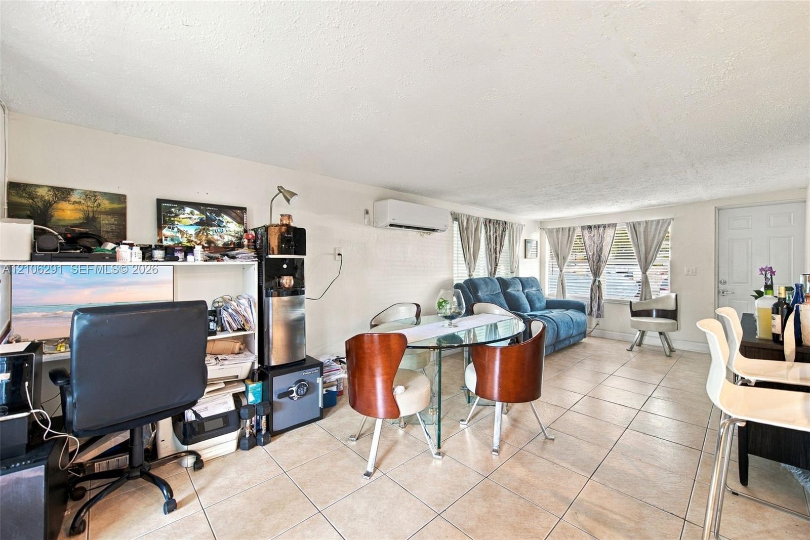 Open-concept interior featuring neutral tile flooring, wall-mounted ductless climate control system, and large windows with horizontal blinds