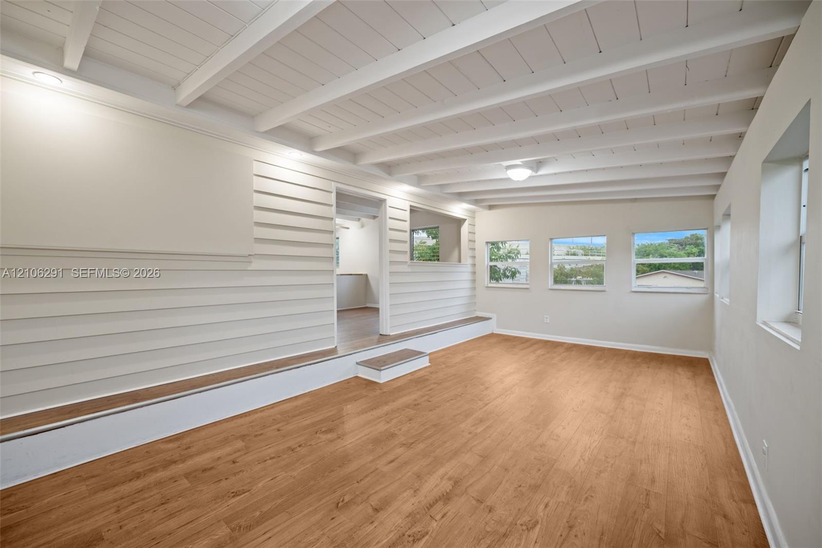 Interior space featuring exposed beam ceilings, wood-finish flooring, horizontal wall paneling, a raised platform level, and multiple windows