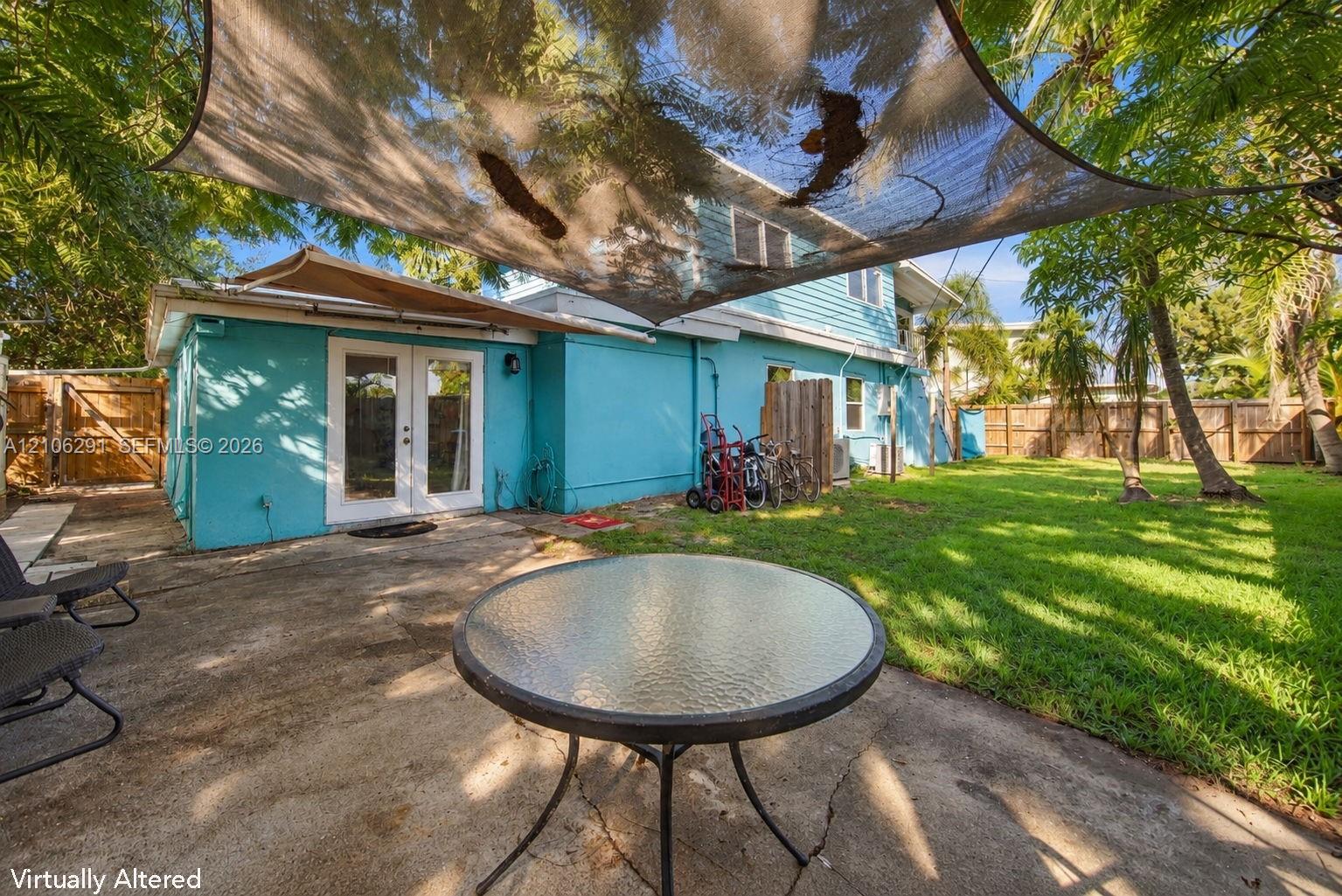 Backyard featuring a concrete patio, shaded seating area with a tensile canopy, mature trees, and perimeter wood fencing
