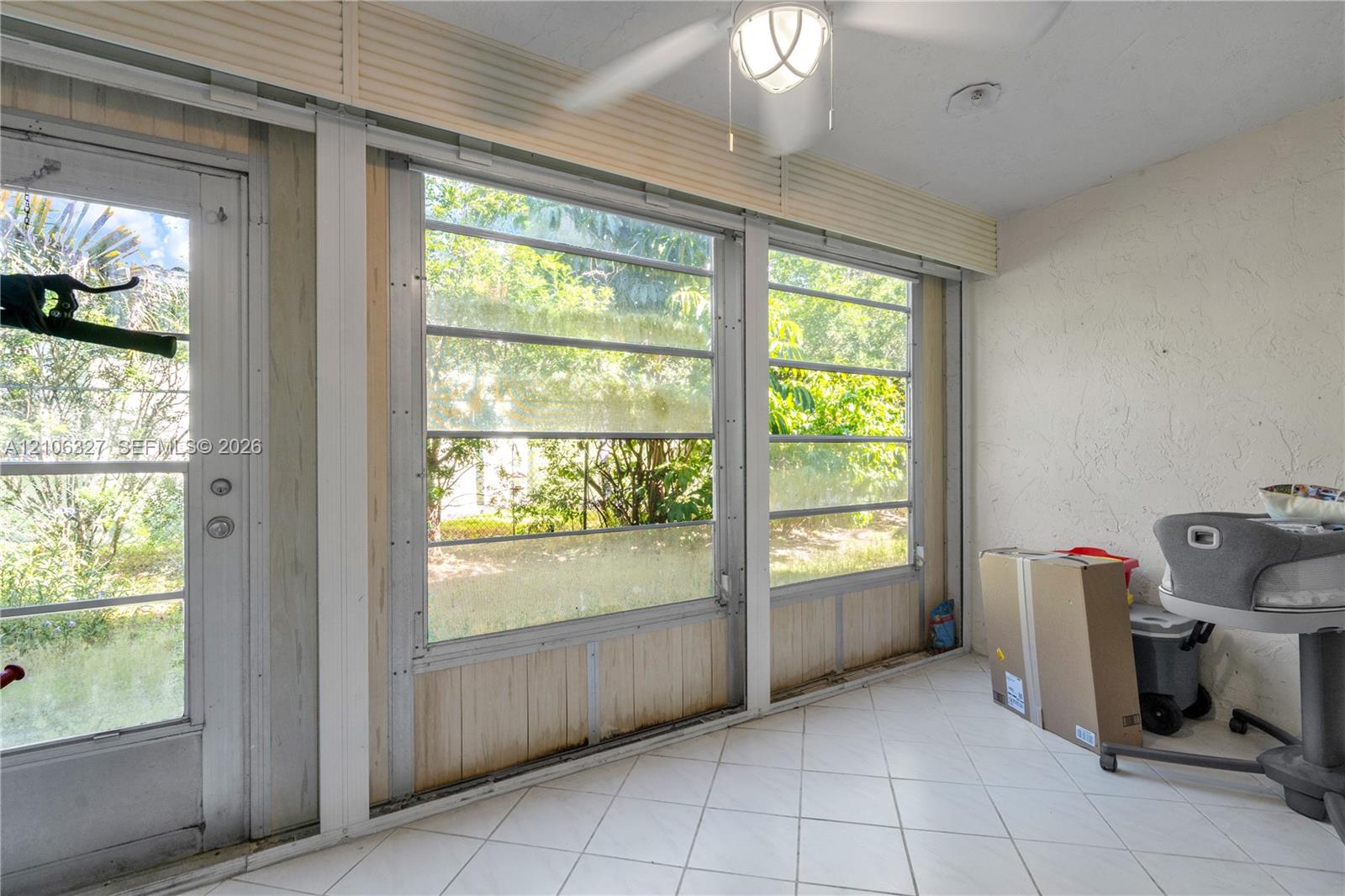 Enclosed sunroom featuring white tile flooring, floor-to-ceiling multi-pane windows, a central ceiling fan with an integrated light fixture, and a glass-paneled exterior door