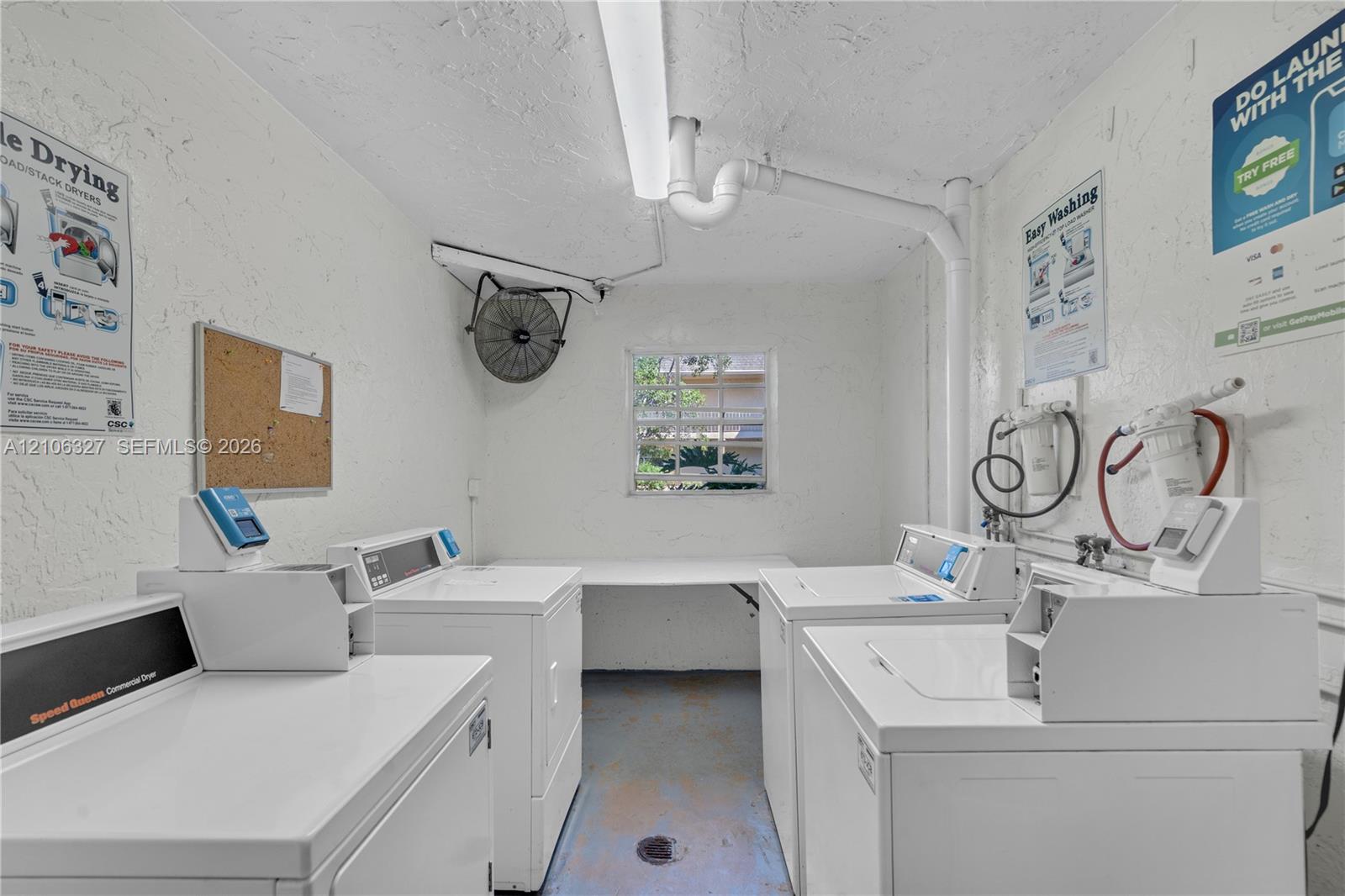 Laundry area featuring commercial-grade washers and dryers, integrated shelving, an exterior-facing window, and wall-mounted exhaust fan