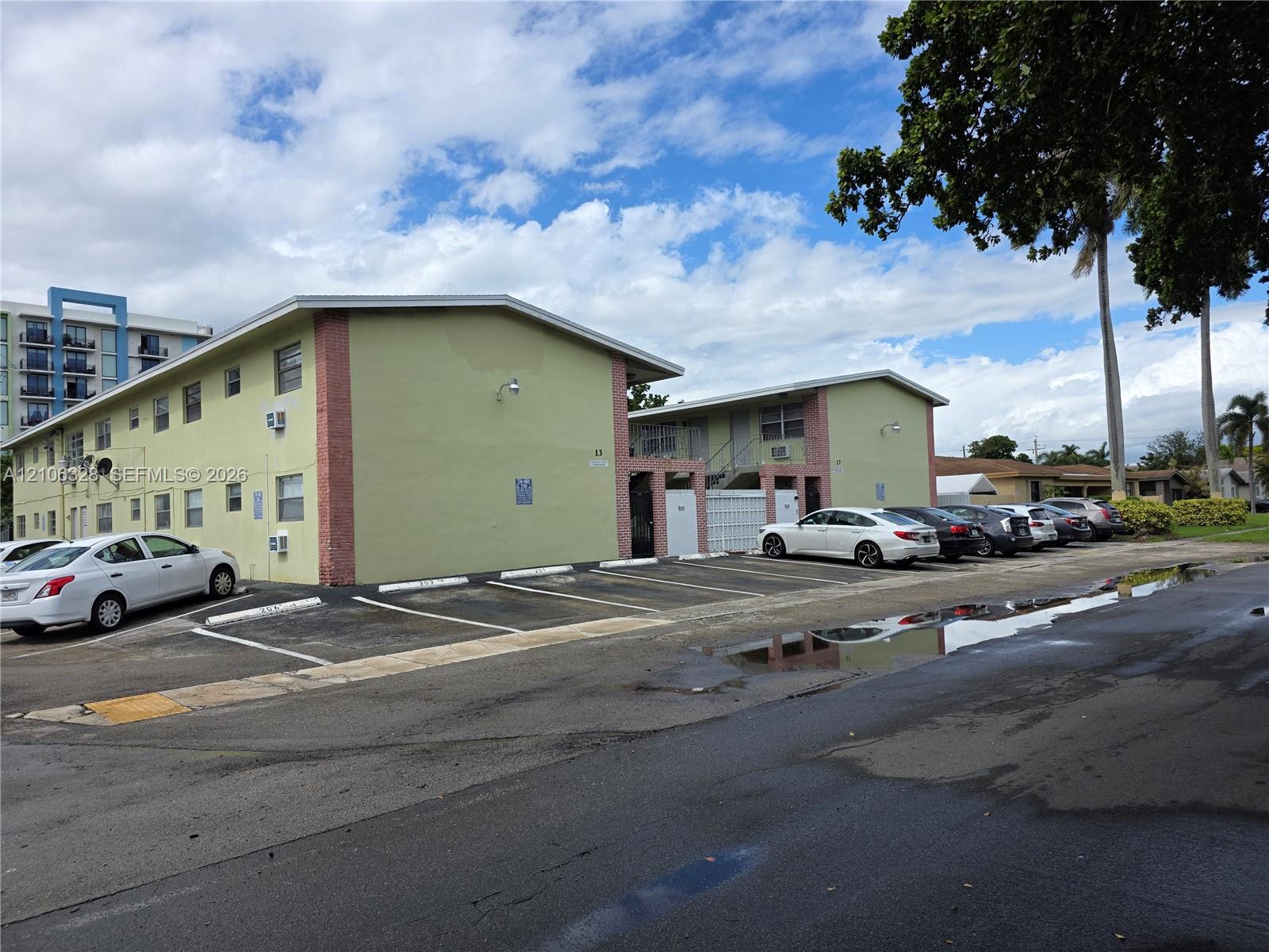 Two-story residential building with stucco exterior, brick corner accents, low-pitch roof, and designated surface parking area Two-story residential building with stucco exterior, brick corner accents, low-pitch roof, and designated surface parking area