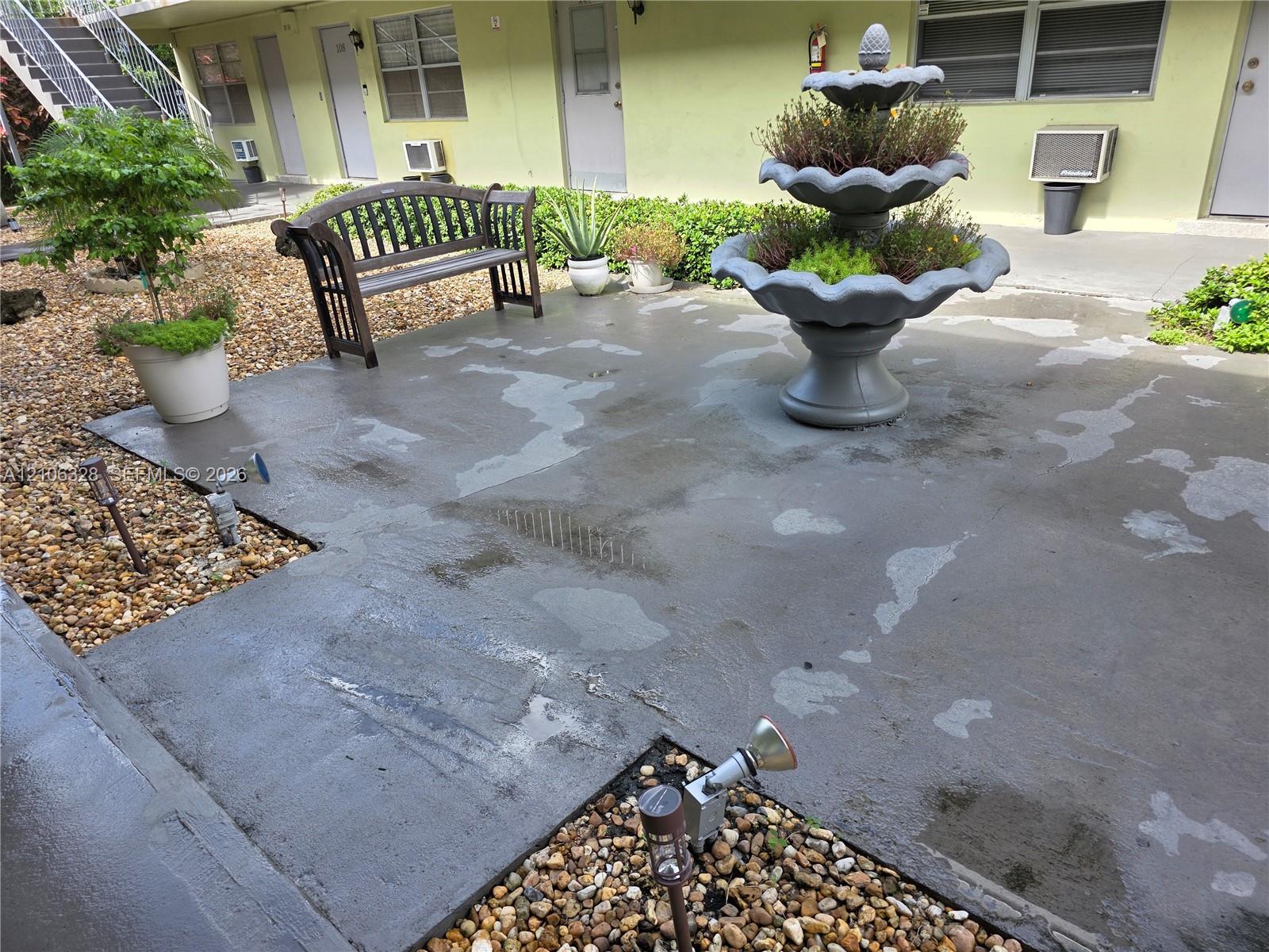 Concrete patio featuring a multi-tiered tiered fountain, gravel landscaping, and metal ground-level accent lighting