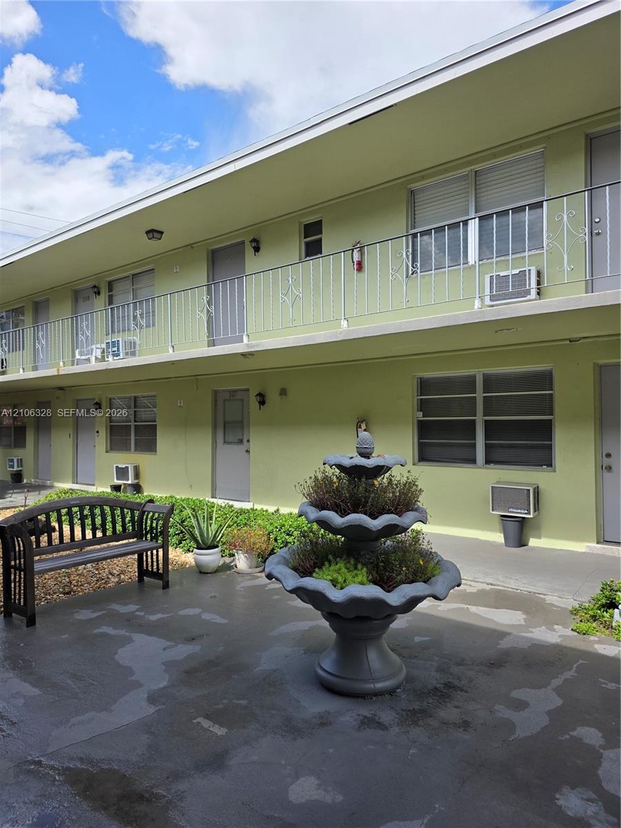 Two-story exterior featuring metal railing, concrete-finish ground level, and decorative multi-tiered stone-finish fountain