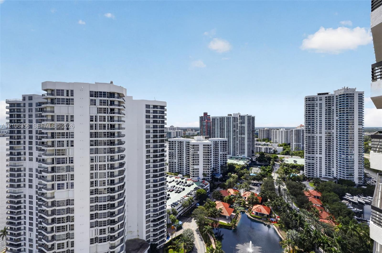 High-rise urban landscape featuring numerous multi-story residential buildings, a water feature with a fountain, and mature tropical landscaping