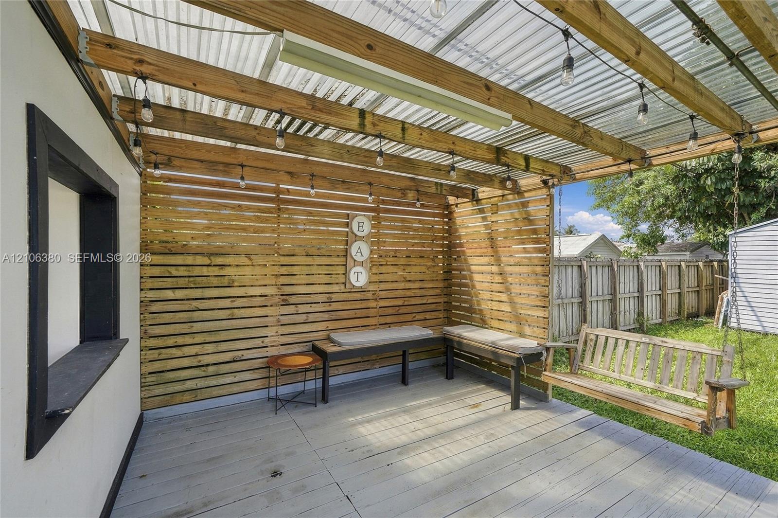 Covered patio featuring a corrugated translucent roof, horizontal wood-slat privacy screen, painted wood decking, and built-in string lighting