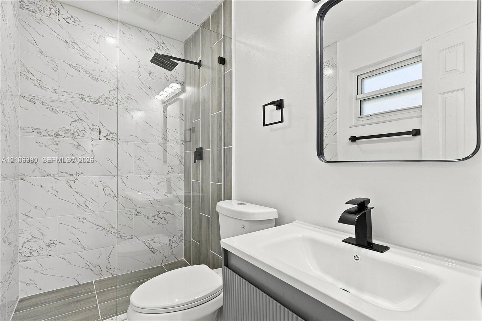 Bathroom featuring a glass-enclosed shower with marbled tile, a rain-style showerhead, wood-finish wall tile accents, a vanity with a rectangular basin and matte black faucet, and a black-framed mirror