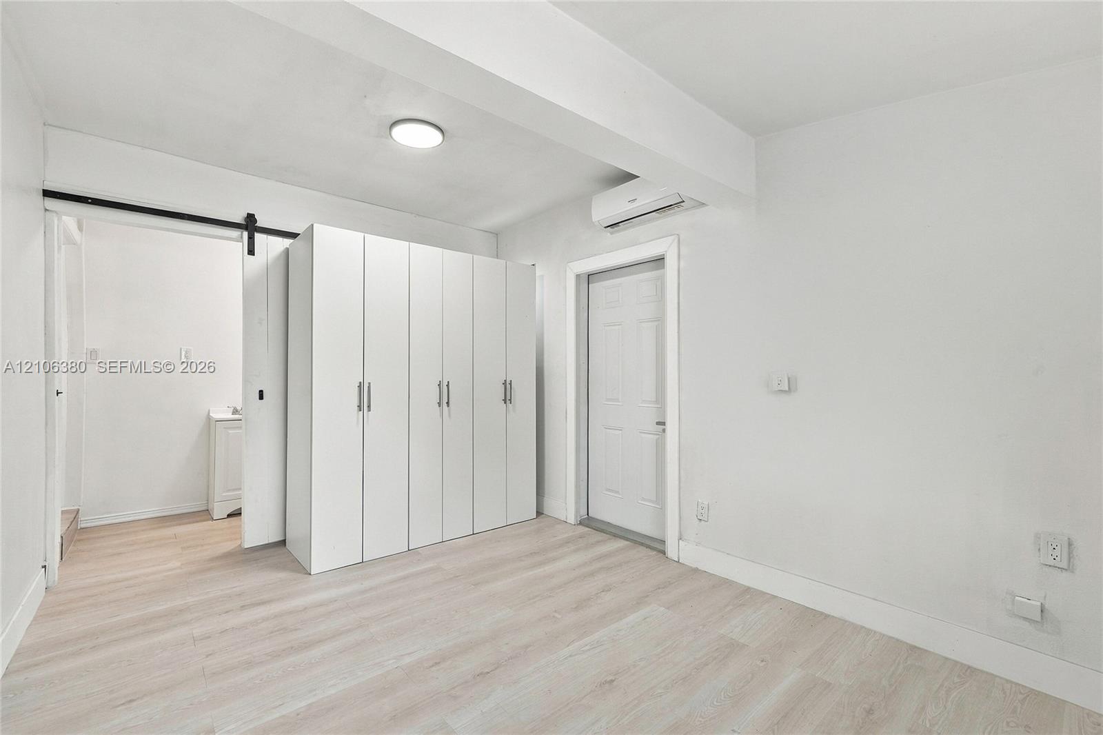 Interior space featuring light-toned wood-finish flooring, white built-in cabinetry, a sliding barn-style door, and a wall-mounted climate control unit