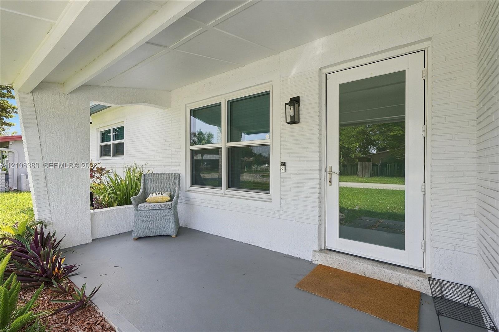 Covered front porch featuring painted brick exterior, concrete flooring, exterior wall-mounted lantern light fixture, and a full-light glass panel entry door