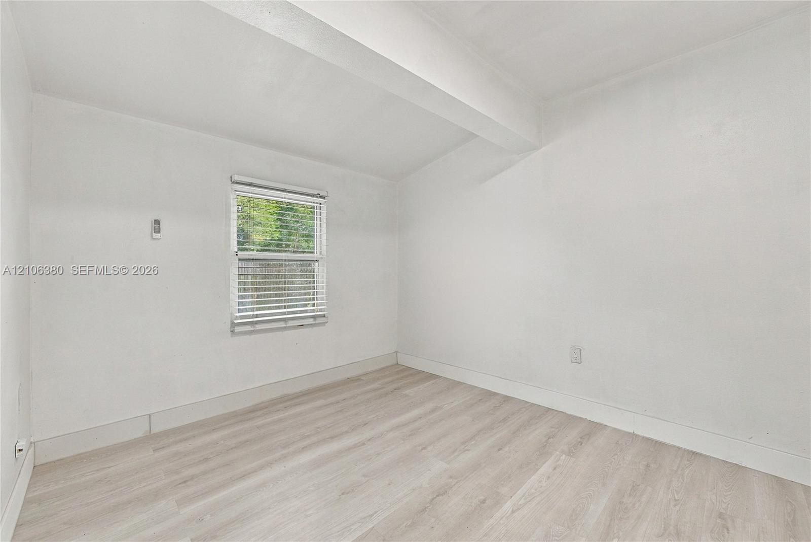Interior room featuring wood-finish flooring, a single-pane window with adjustable blinds, and smooth-finish walls