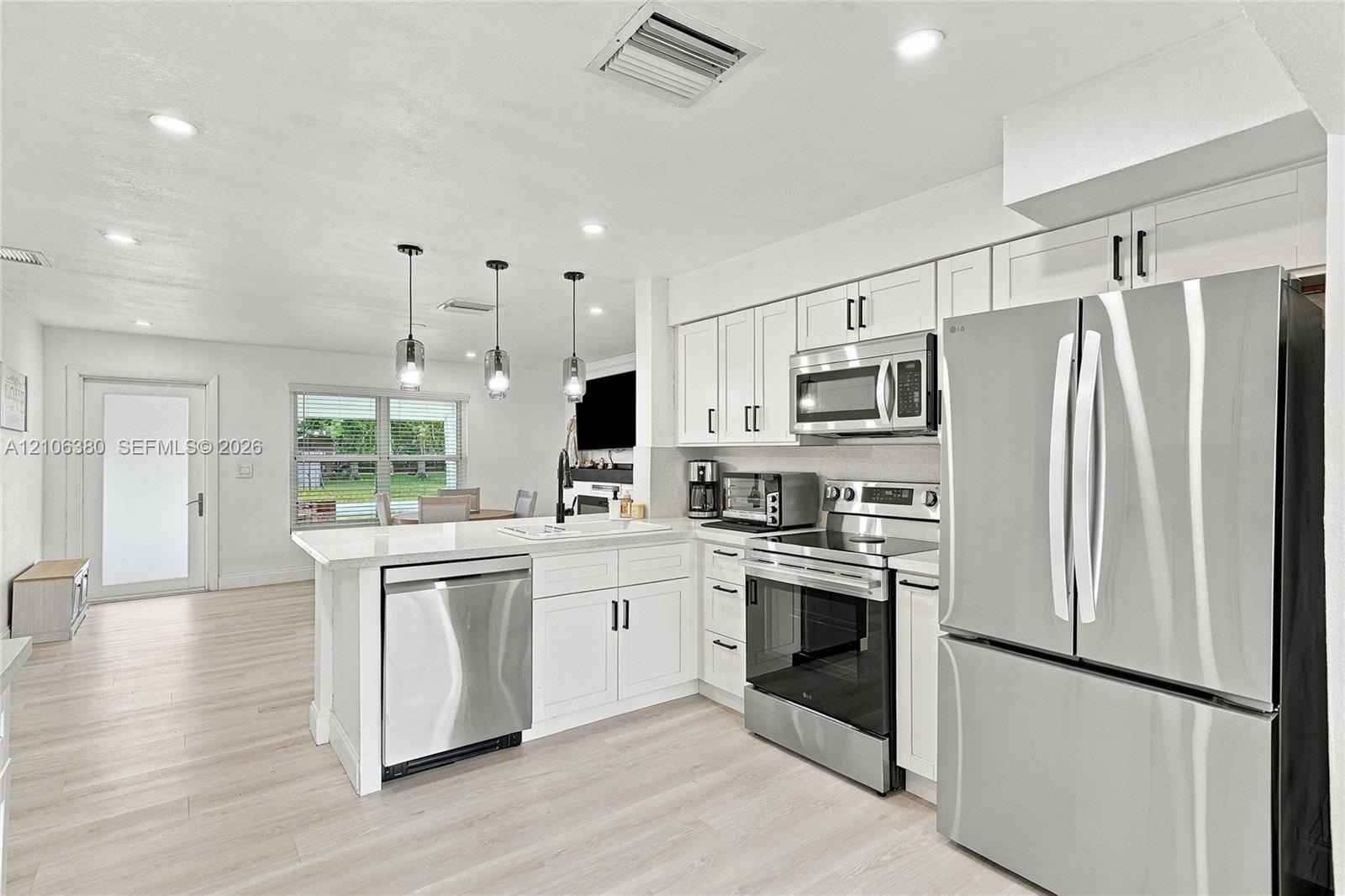 Kitchen featuring white shaker-style cabinetry, stainless steel appliances, quartz countertops, a peninsula with pendant lighting, and light-toned wood-finish flooring