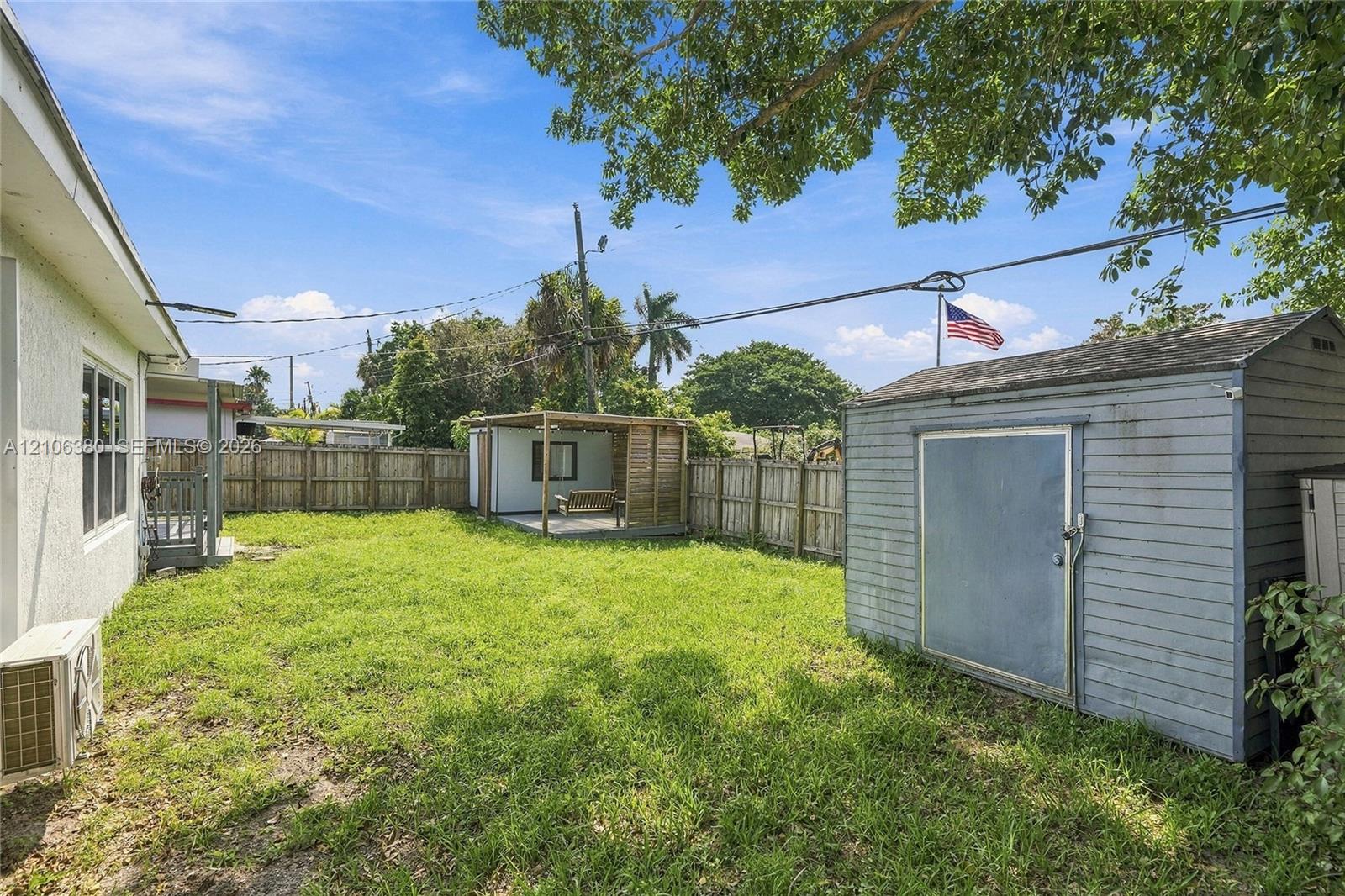 Fenced backyard featuring a grass lawn, detached storage structure, and covered outdoor area