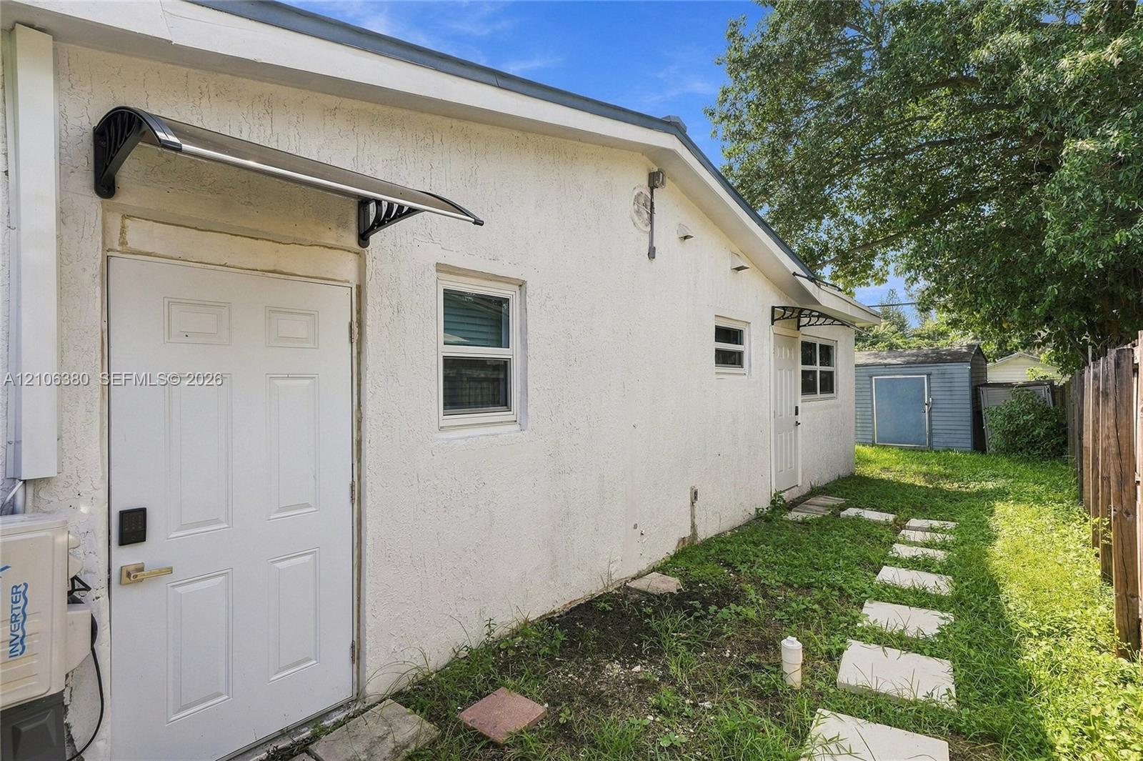 Exterior side profile featuring stucco siding, two entry doors with overhead metal awnings, multi-pane windows, and a paved stone pathway