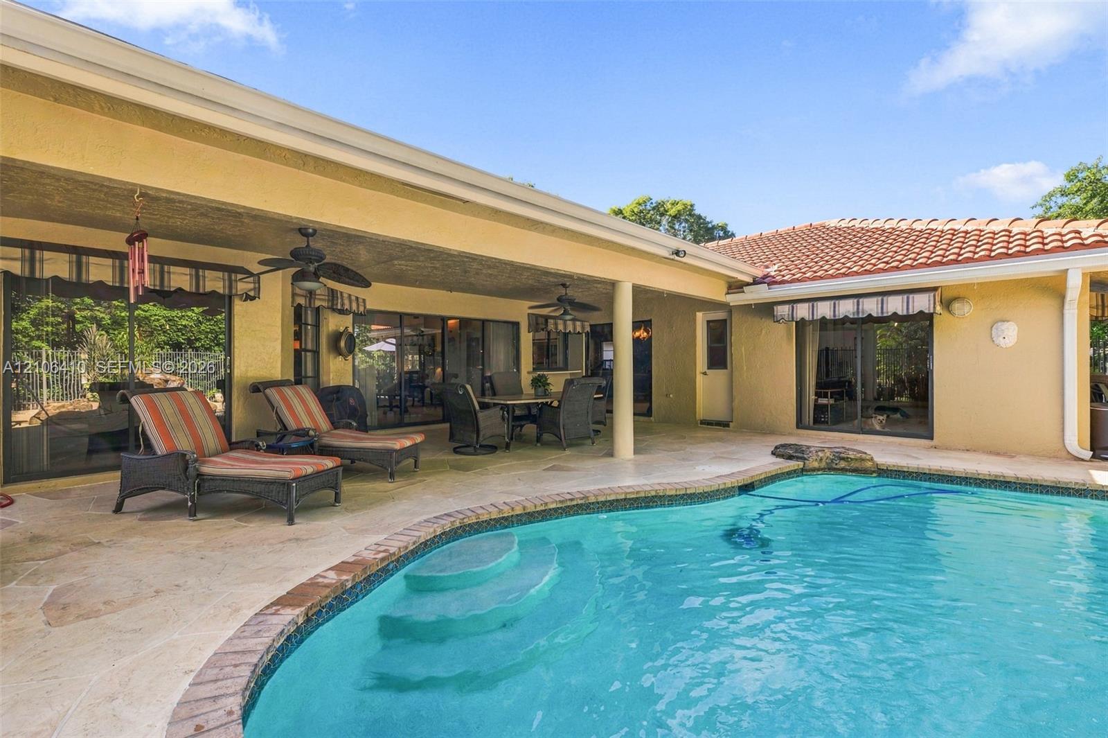 Covered lanai featuring natural stone flooring, recessed ceiling fans, and an inground pool with tile surround
