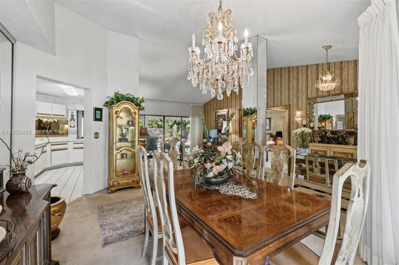 Dining area featuring vaulted ceilings, a central crystal chandelier, floor-to-ceiling mirror paneling, and textured wallpaper