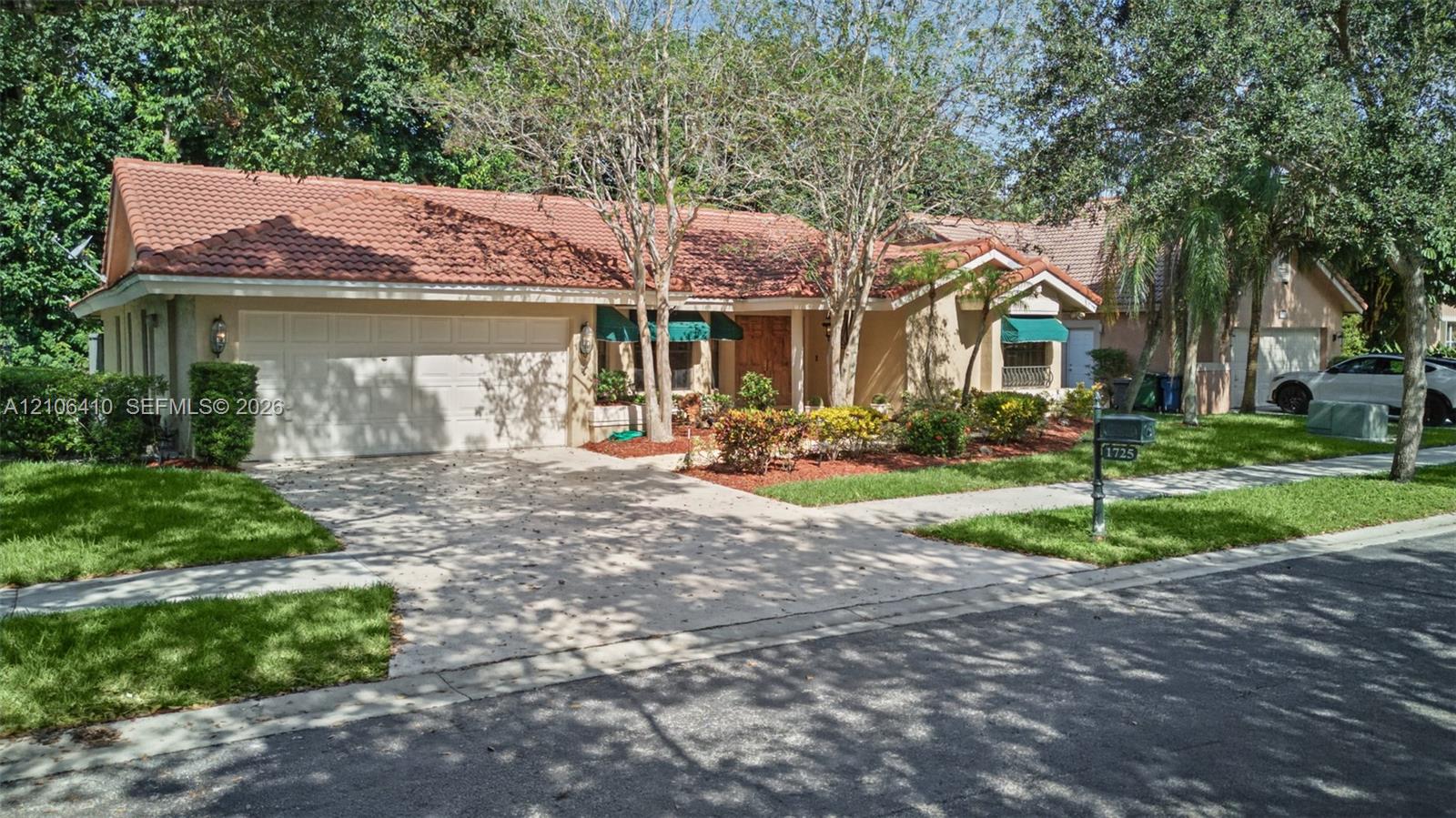 Single-story exterior featuring a clay tile roof, stucco facade, two-car garage, and established landscaping