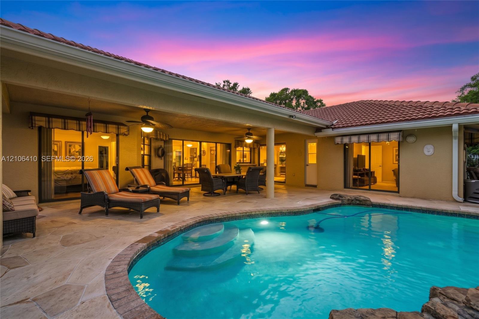 Covered patio featuring stone-tiled flooring and dual ceiling fans, paired with an inground pool with built-in steps and rock-feature masonry