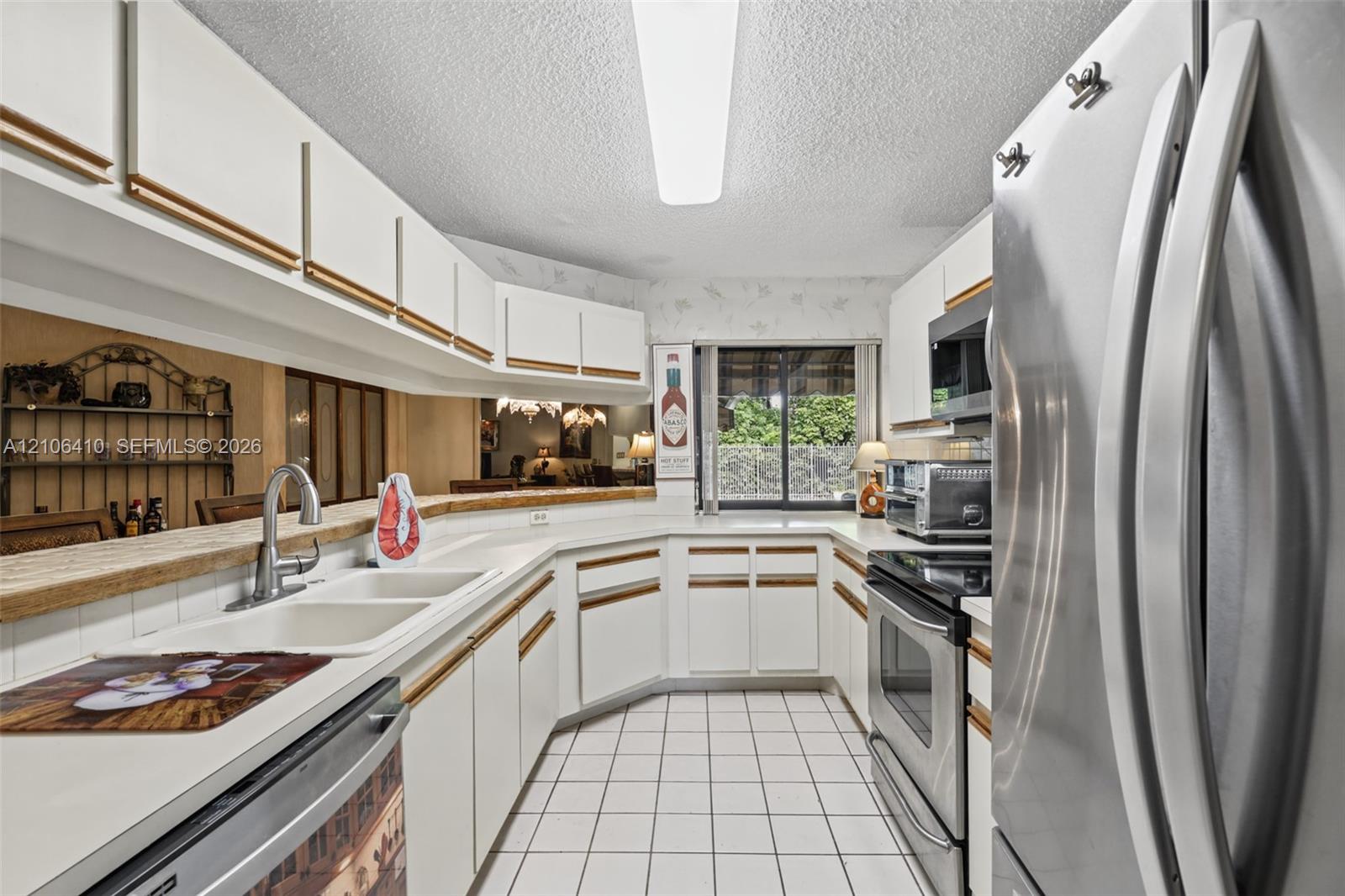 Kitchen featuring white cabinetry, stainless steel appliances, a dual-basin sink with a gooseneck faucet, tile flooring, and a breakfast bar