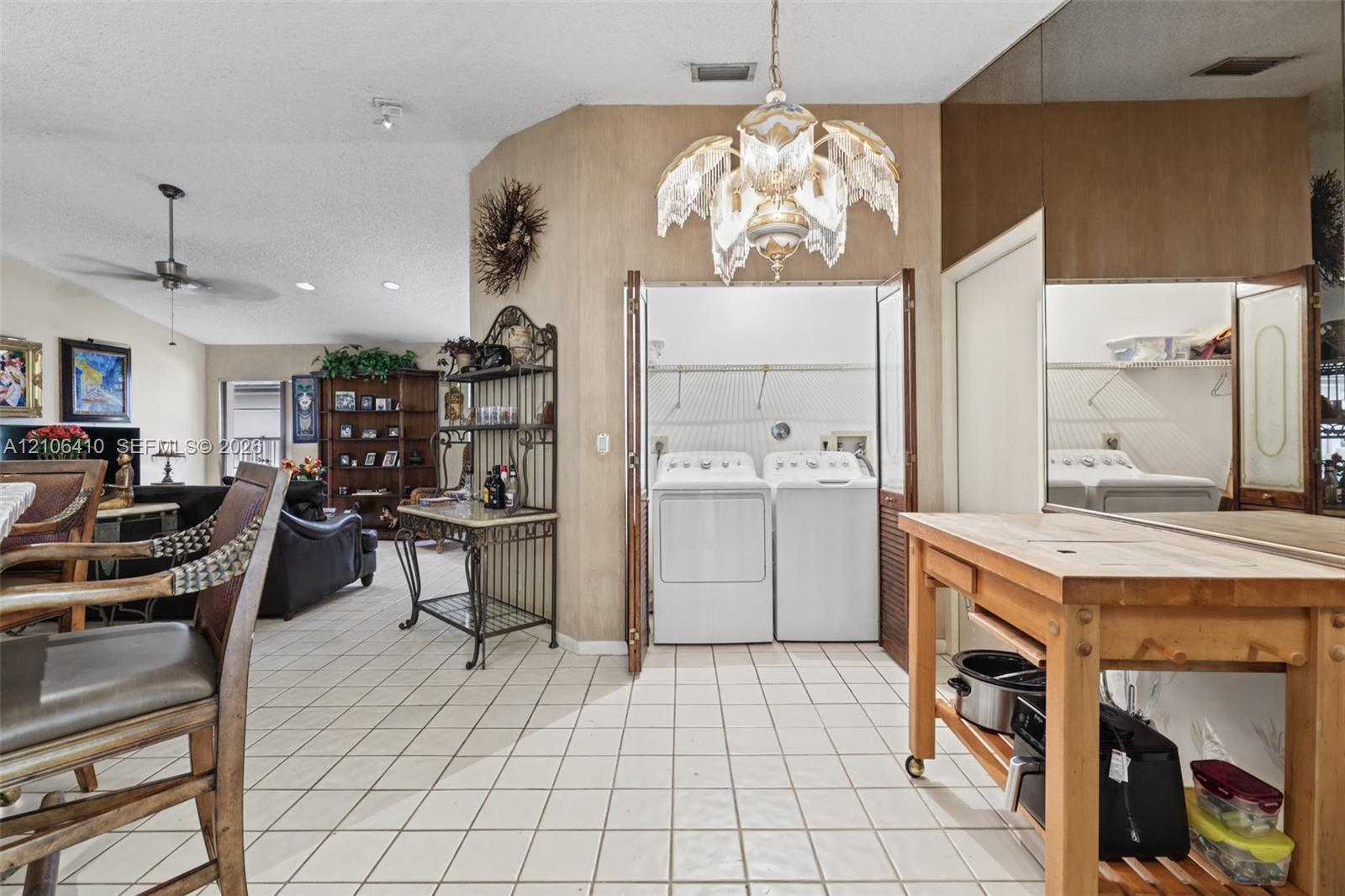 Ceramic tile flooring, vaulted ceilings, and built-in laundry closet with bi-fold doors, accented by decorative chandelier lighting and mirrored wall paneling