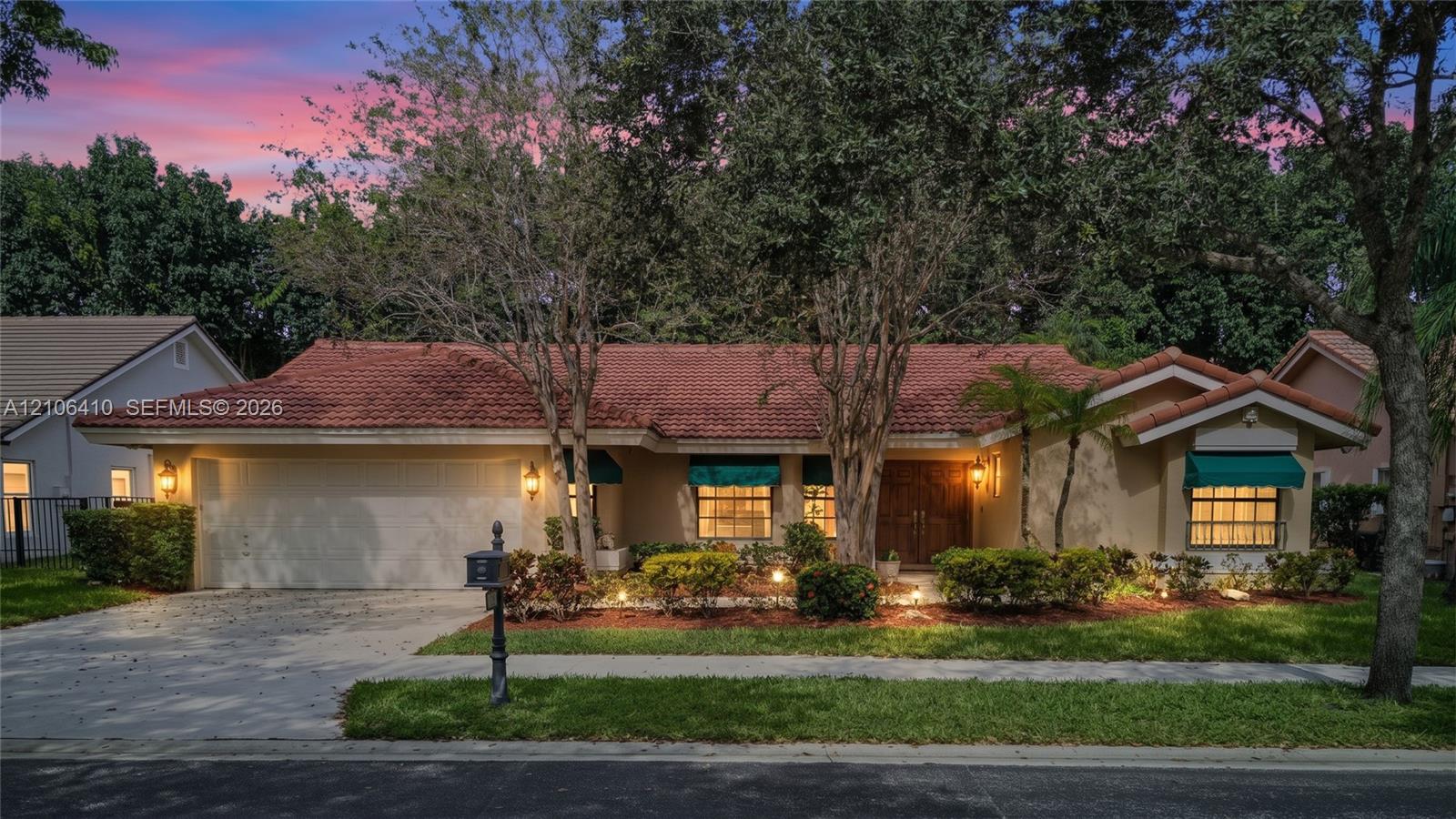 Single-story residence featuring a tile roof, dual-car garage, stone-paved driveway, and exterior window awnings