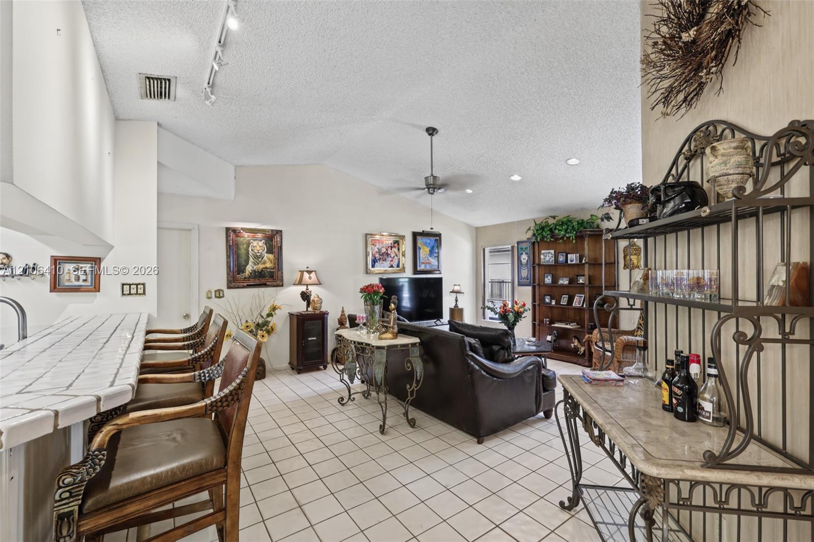 Living area featuring vaulted ceilings, tile flooring, and a built-in kitchen peninsula with a tiled countertop and breakfast bar seating