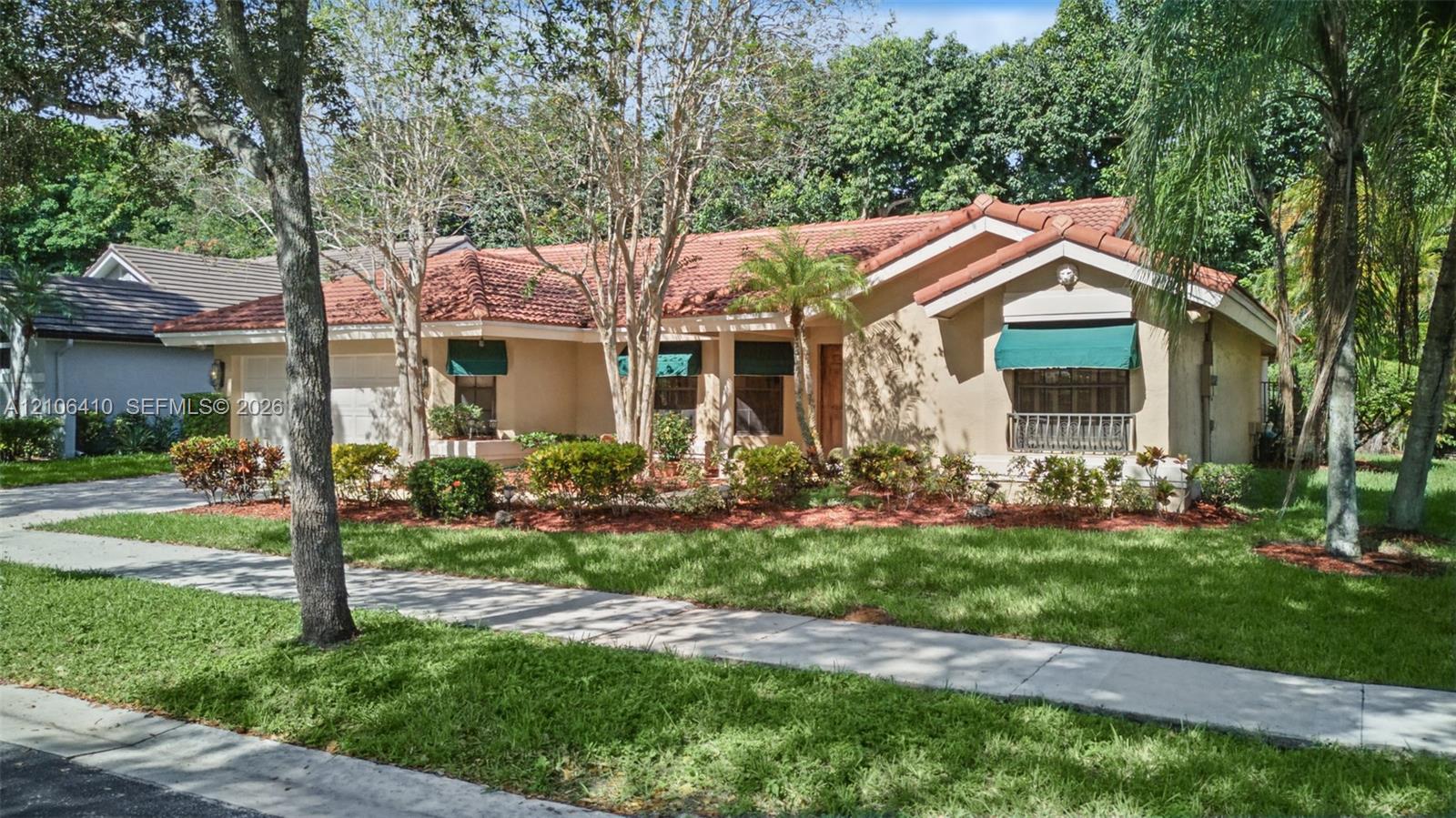 Stucco exterior featuring a terracotta tile roof, fixed-frame window awnings, and landscaped garden beds