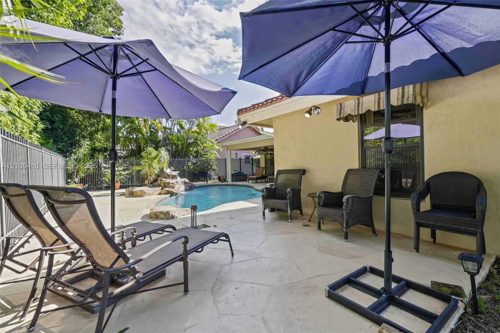Outdoor living area featuring a paved stone patio, a swimming pool with a rock-style water feature, and a stucco exterior finish