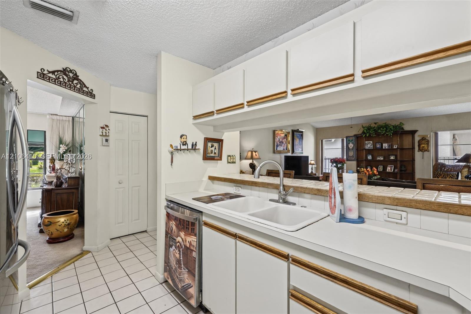 Kitchen featuring white cabinetry with wood trim, white tile countertops, dual-basin sink, and ceramic tile flooring