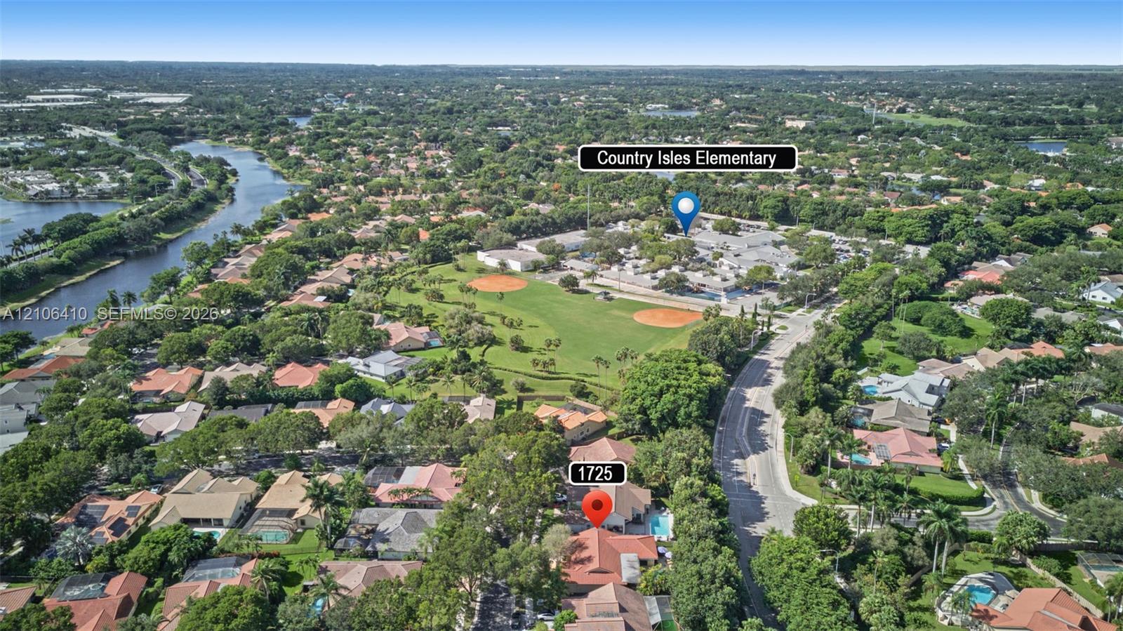 Aerial perspective of residential property featuring a tiled roof, private swimming pool, mature canopy trees, and proximity to expansive green space and water frontage