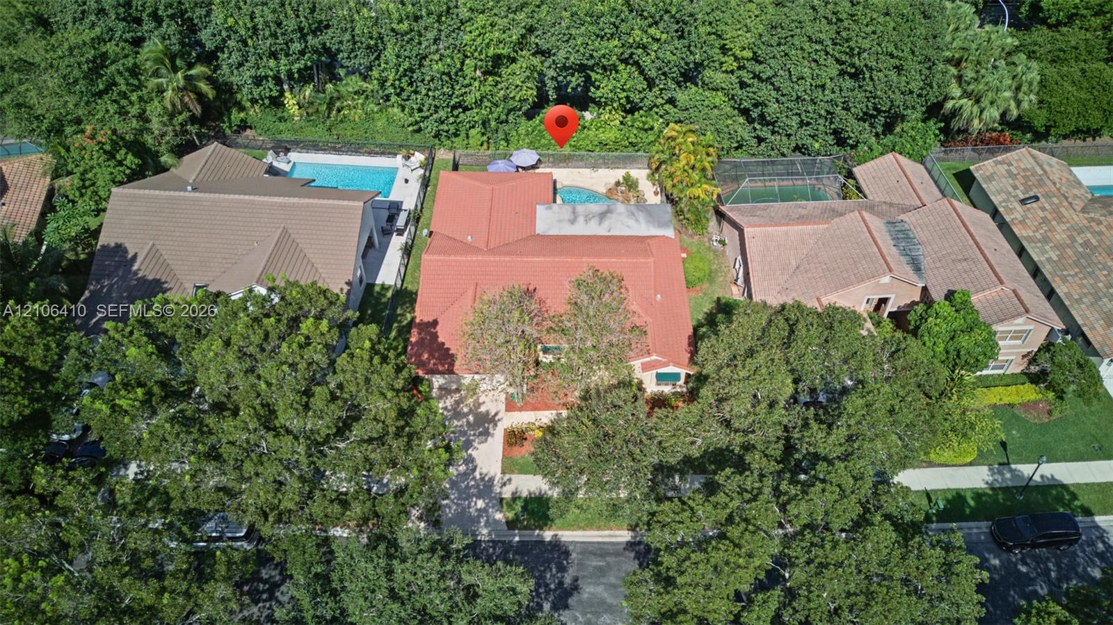 Aerial perspective featuring a tile roof, an in-ground swimming pool, mature tree canopy, and dense perimeter landscaping