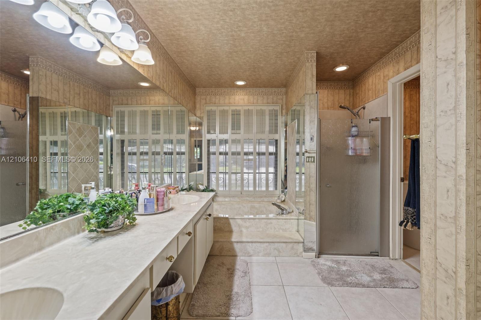 Dual-sink vanity with integrated countertop, recessed lighting, glass-enclosed shower, built-in soaking tub with surround, and large-format tile flooring