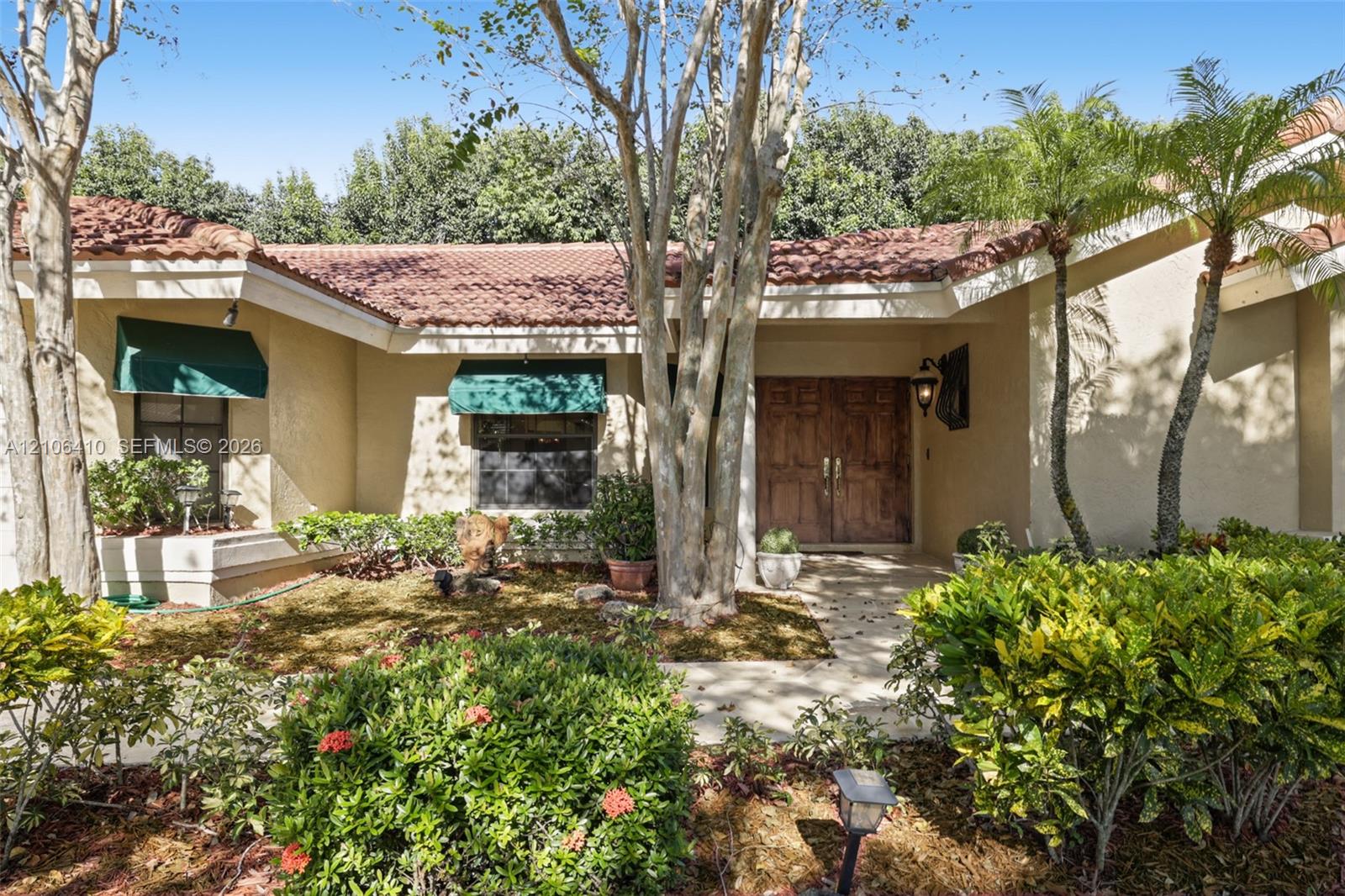 Stucco exterior featuring a clay tile roof, double-door entry, and decorative canvas window awnings