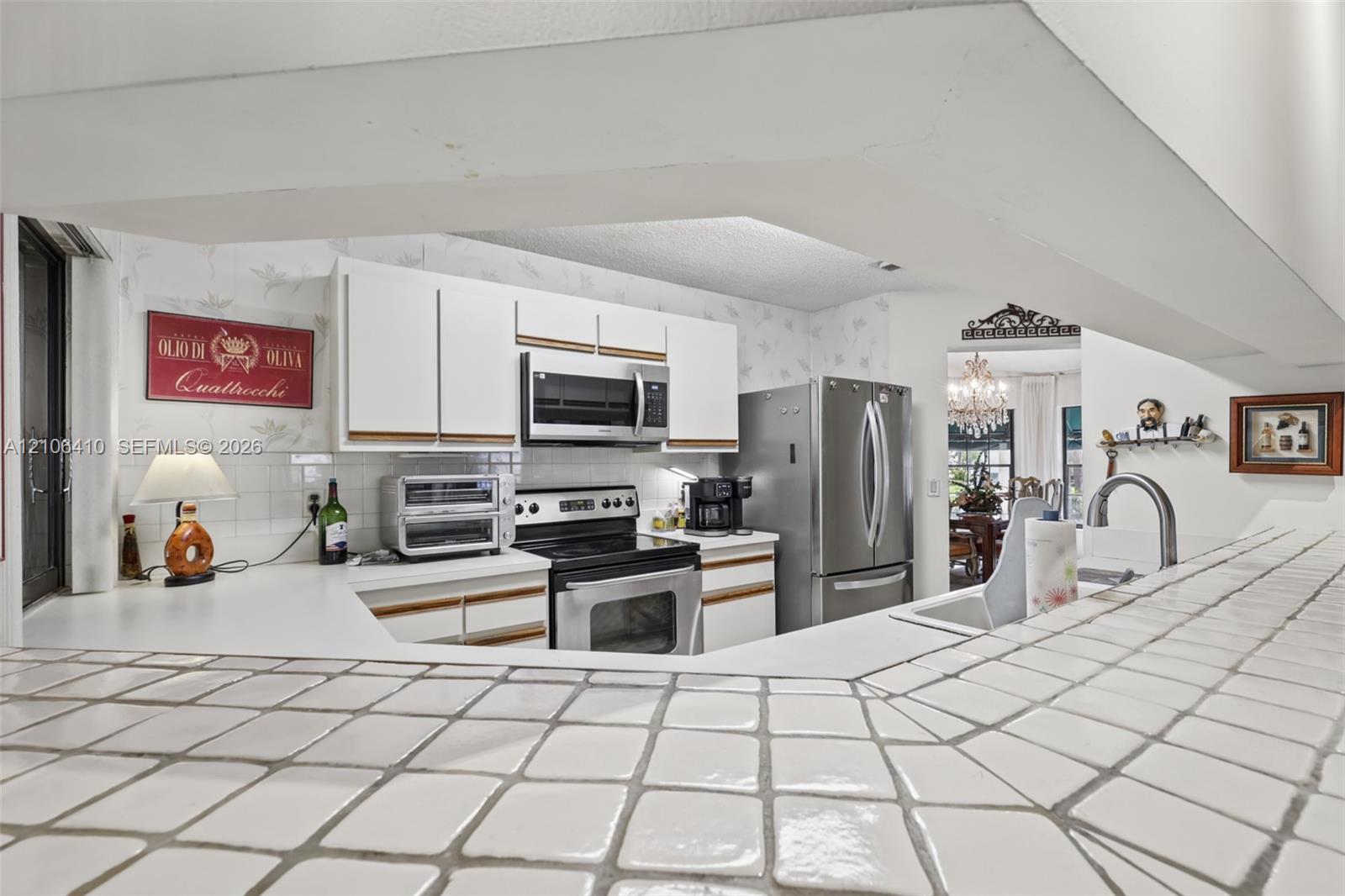 Kitchen featuring white cabinetry, tiled countertop, stainless steel appliances, and a built-in kitchen sink with a gooseneck faucet