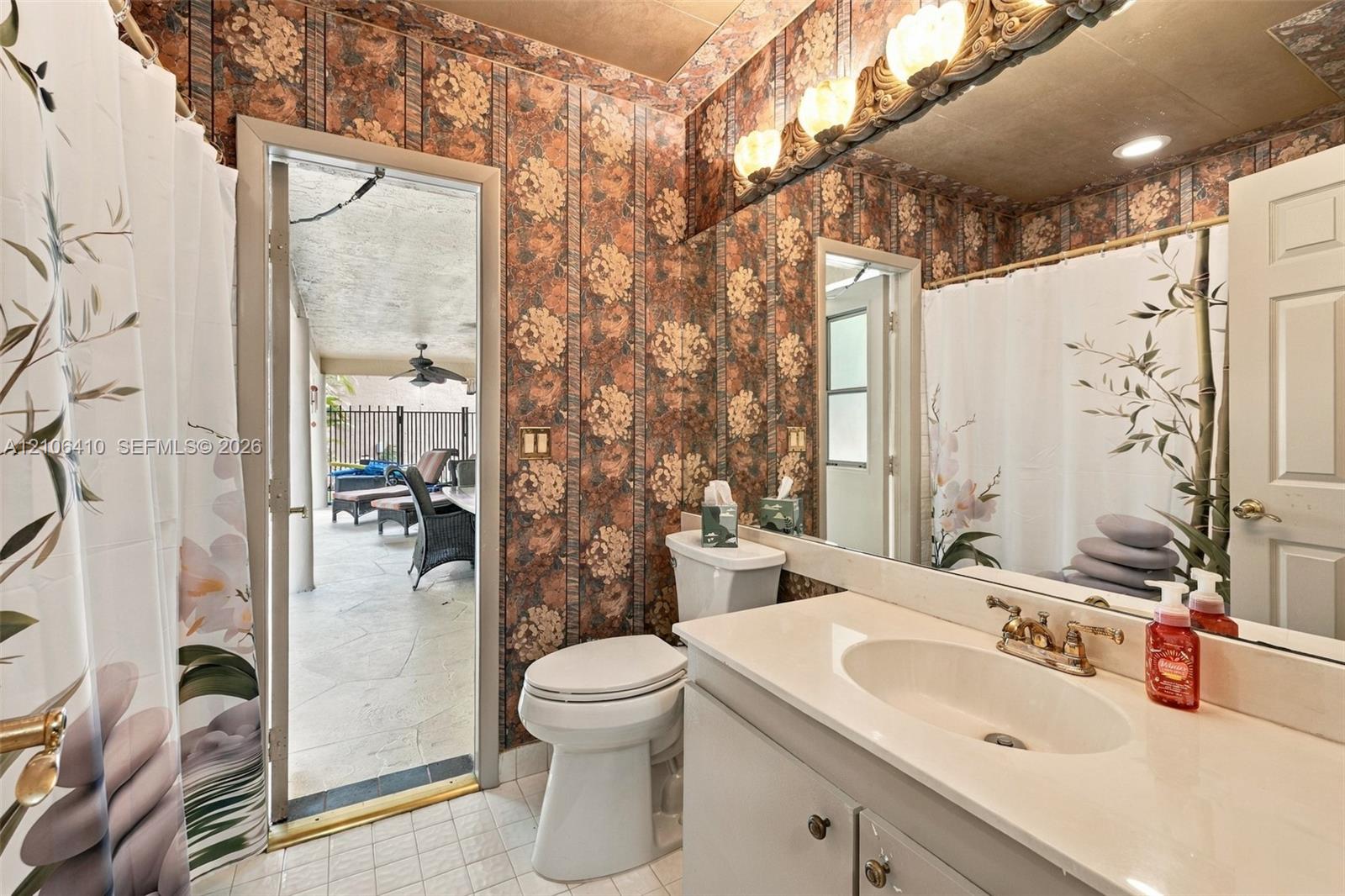 Bathroom featuring a solid-surface vanity countertop, drop-in sink with dual-handle faucet, full-width wall mirror, decorative light fixture, and tile flooring