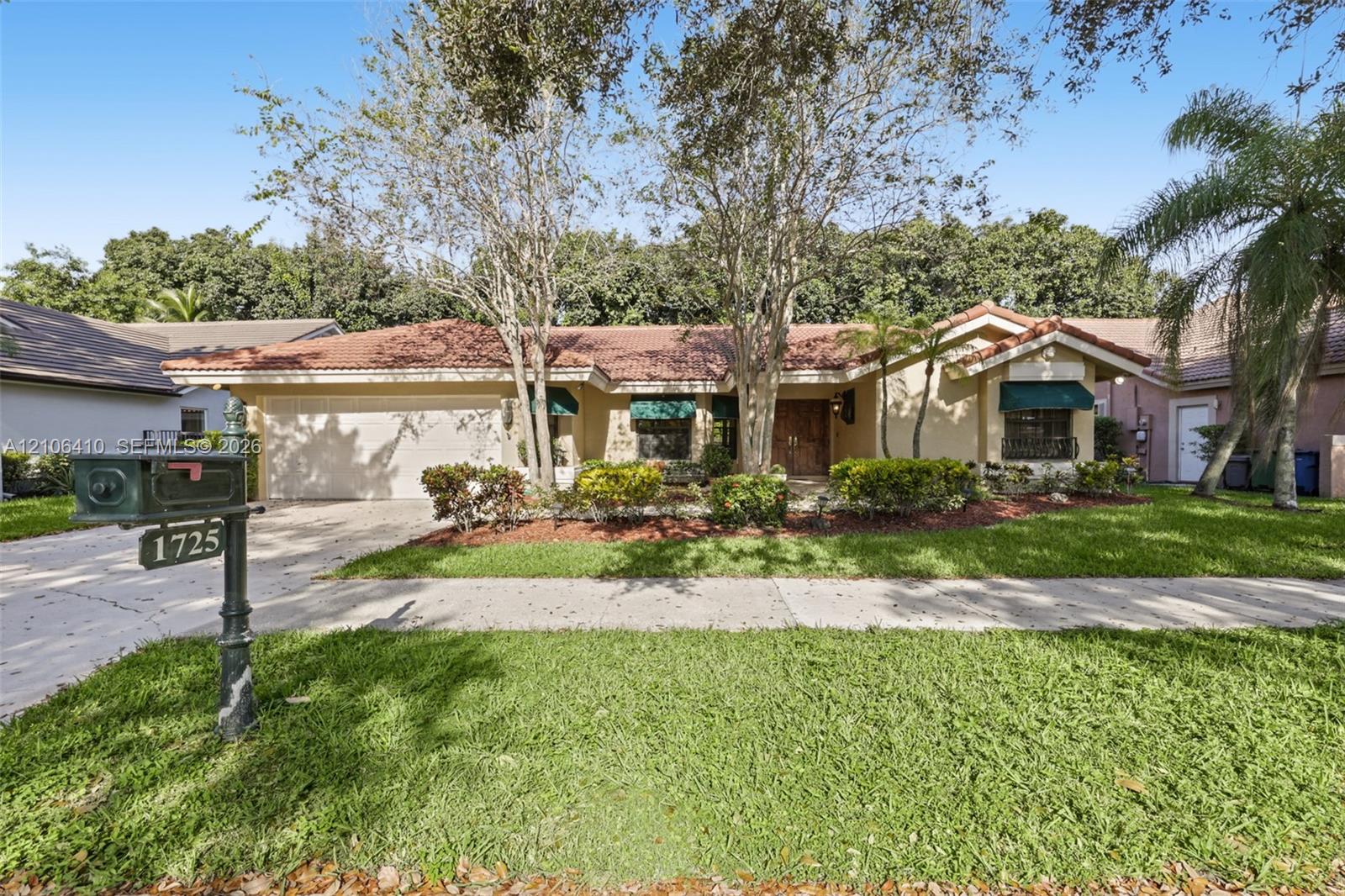 Single-story exterior featuring a multi-gabled tile roof, stucco facade, attached two-car garage, and established landscaping with mature shade trees
