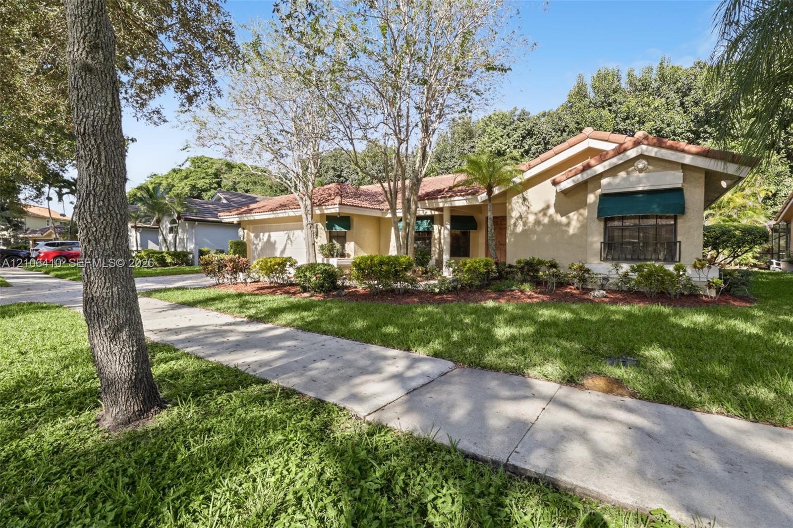 Stucco exterior featuring a clay tile roof, attached garage, and decorative window awnings, complemented by established landscaping