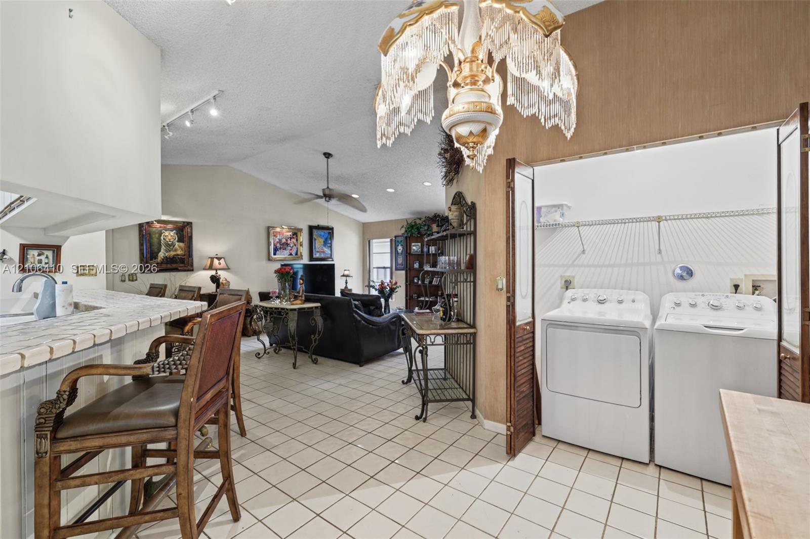 Vaulted ceiling with decorative chandelier, tile flooring, and integrated laundry closet with bifold doors