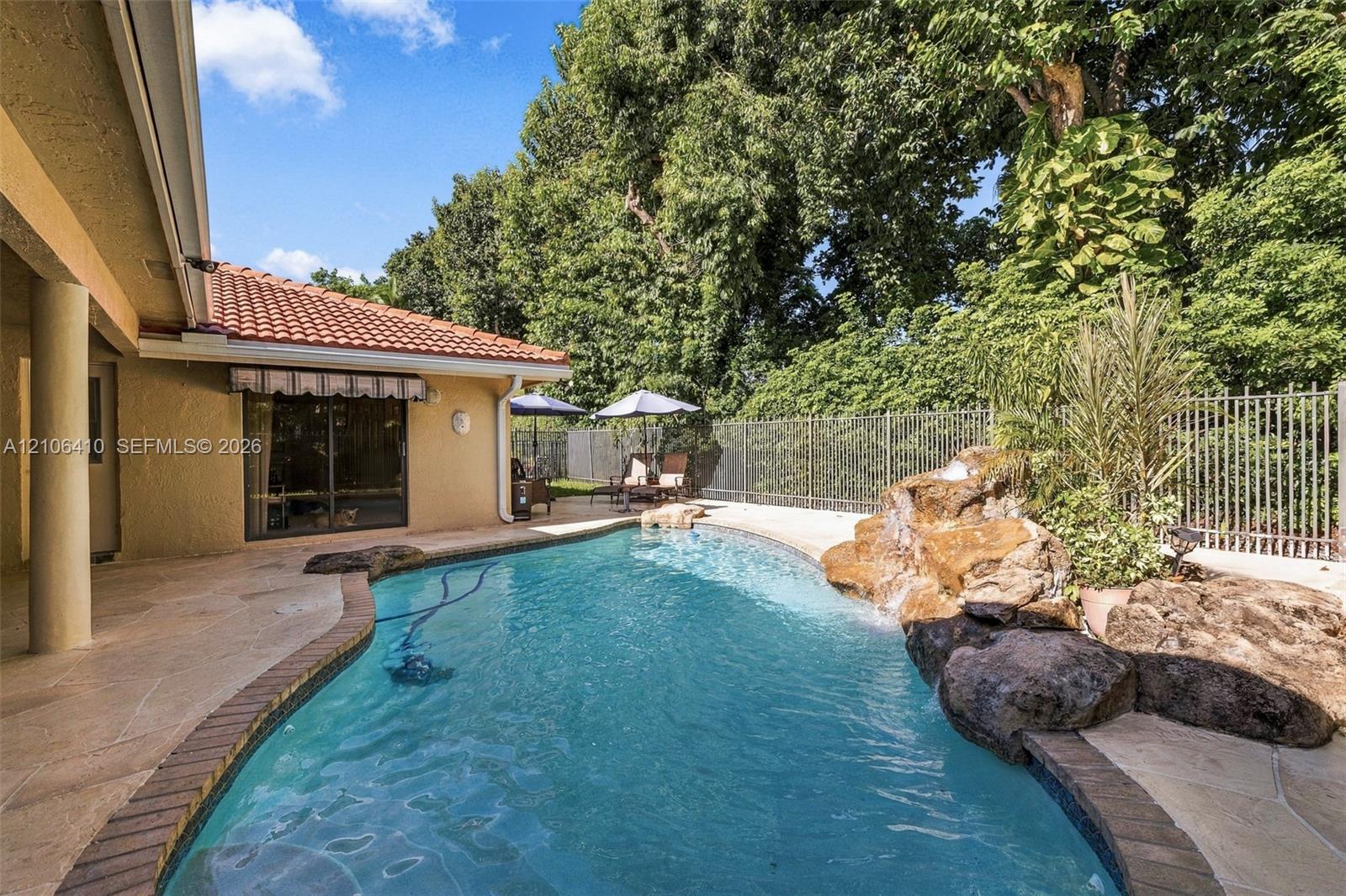 Backyard featuring an inground pool with a rock water feature, stone-finished patio, tile roof, and metal perimeter fencing
