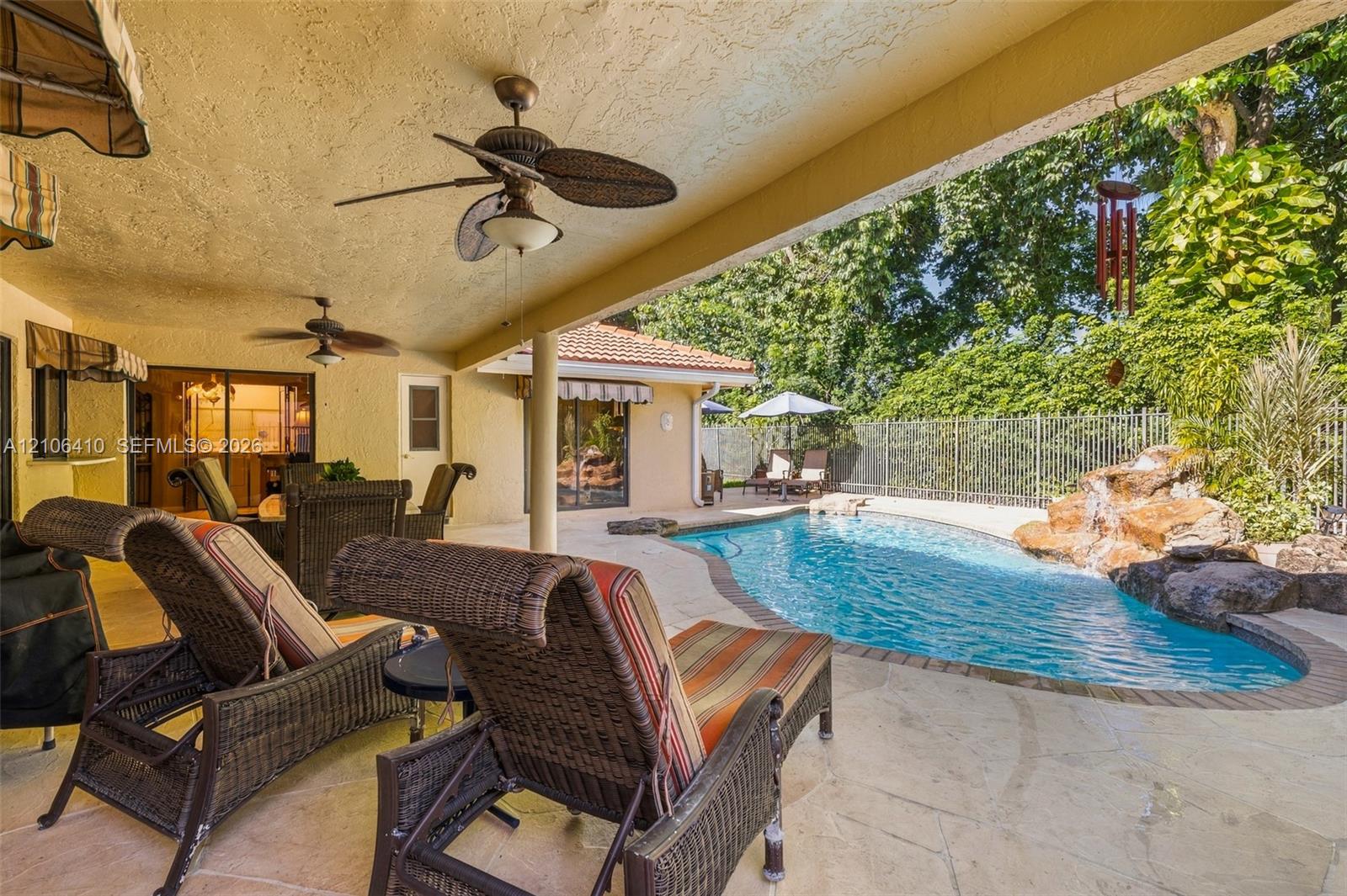 Covered patio featuring a textured ceiling with integrated paddle fans, stone-paver decking, and a free-form pool with a rock water feature