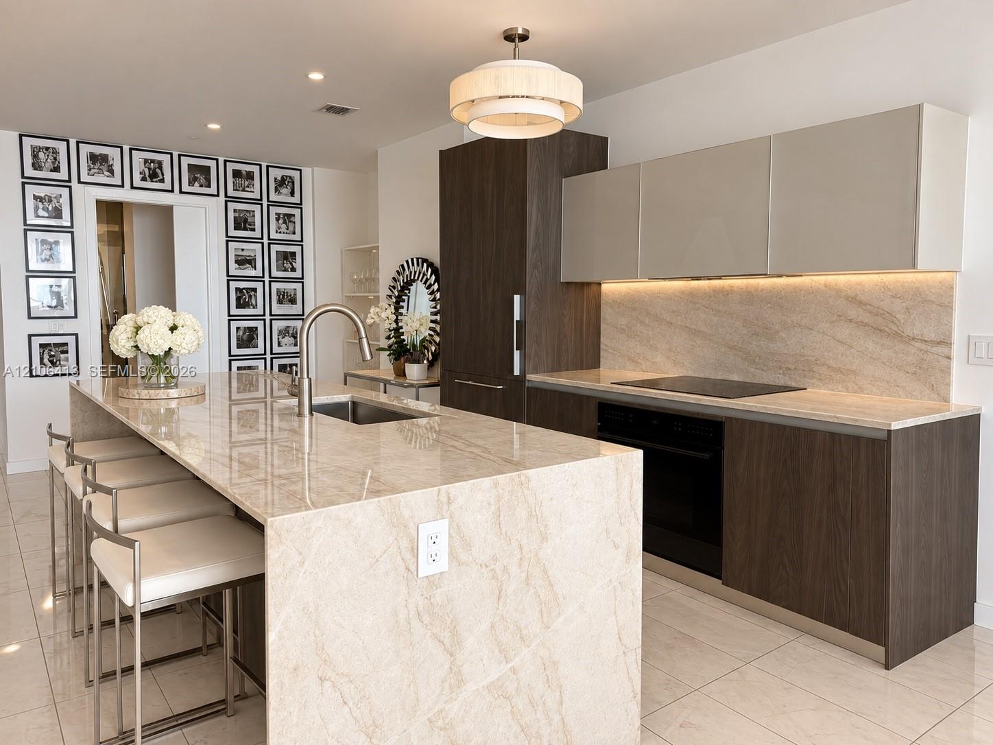 Kitchen featuring a stone-topped island with an integrated sink, custom two-tone cabinetry, recessed under-cabinet lighting, a built-in induction cooktop, and polished tile flooring