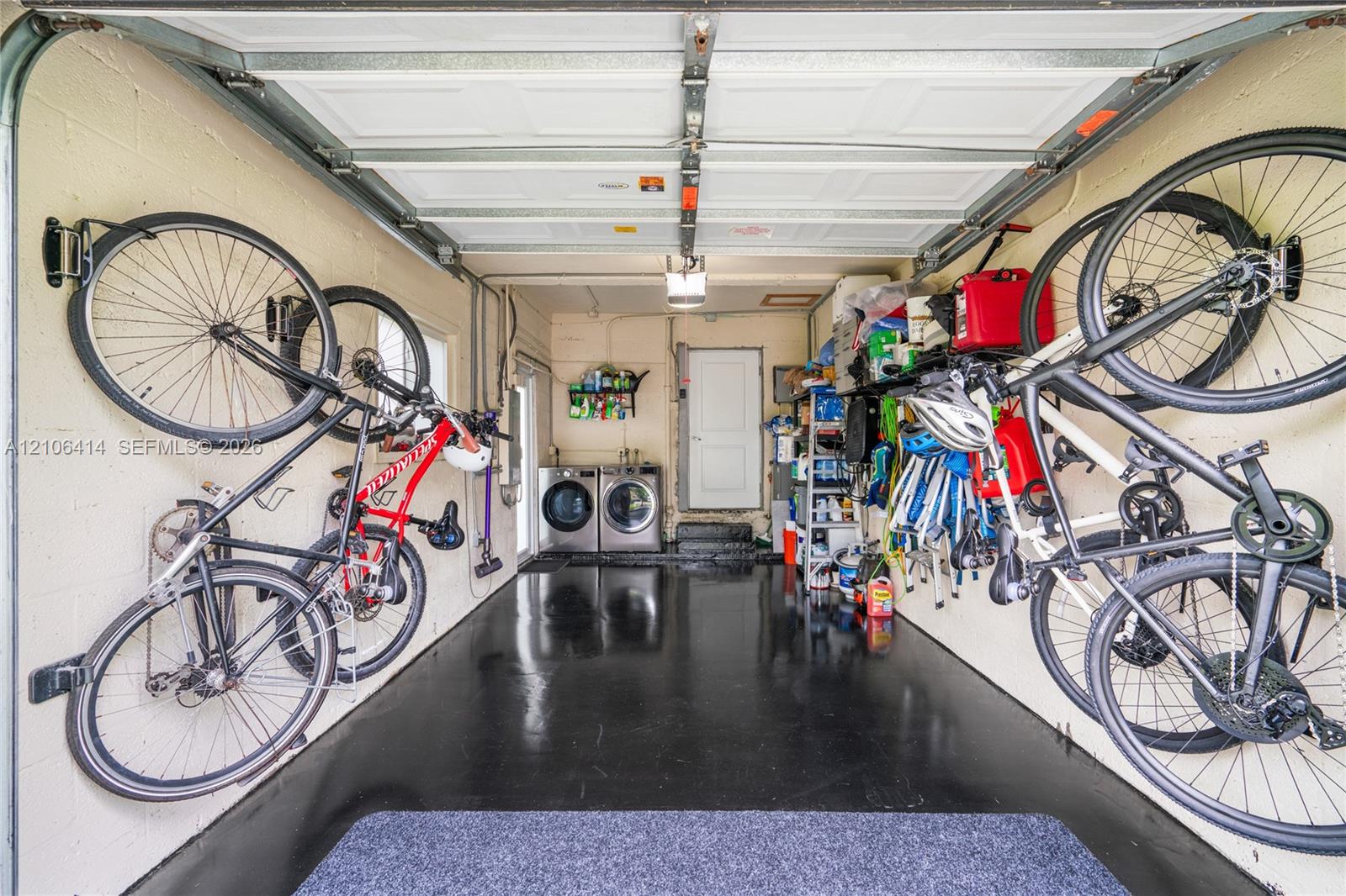Garage featuring a high-gloss epoxy floor coating, white masonry walls, overhead garage door system, and dedicated laundry area with side-by-side washer and dryer