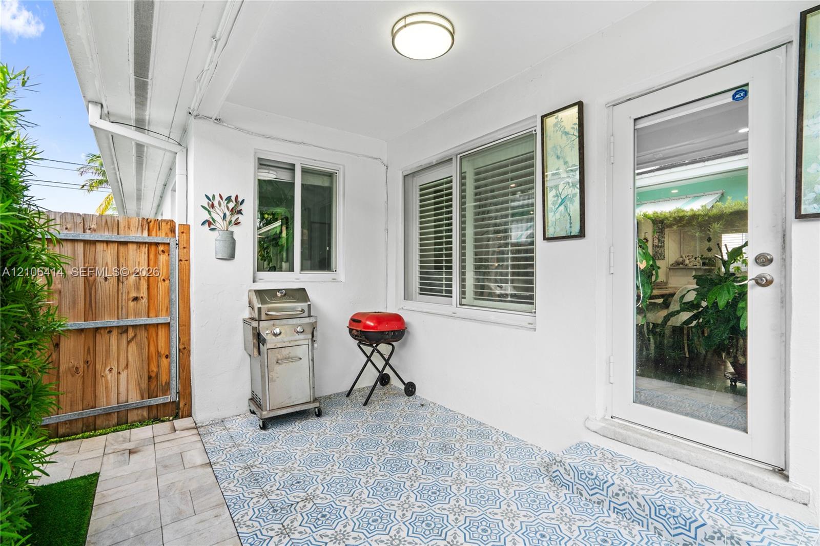 Covered patio featuring patterned tile flooring, a half-glass entry door, and white stucco walls