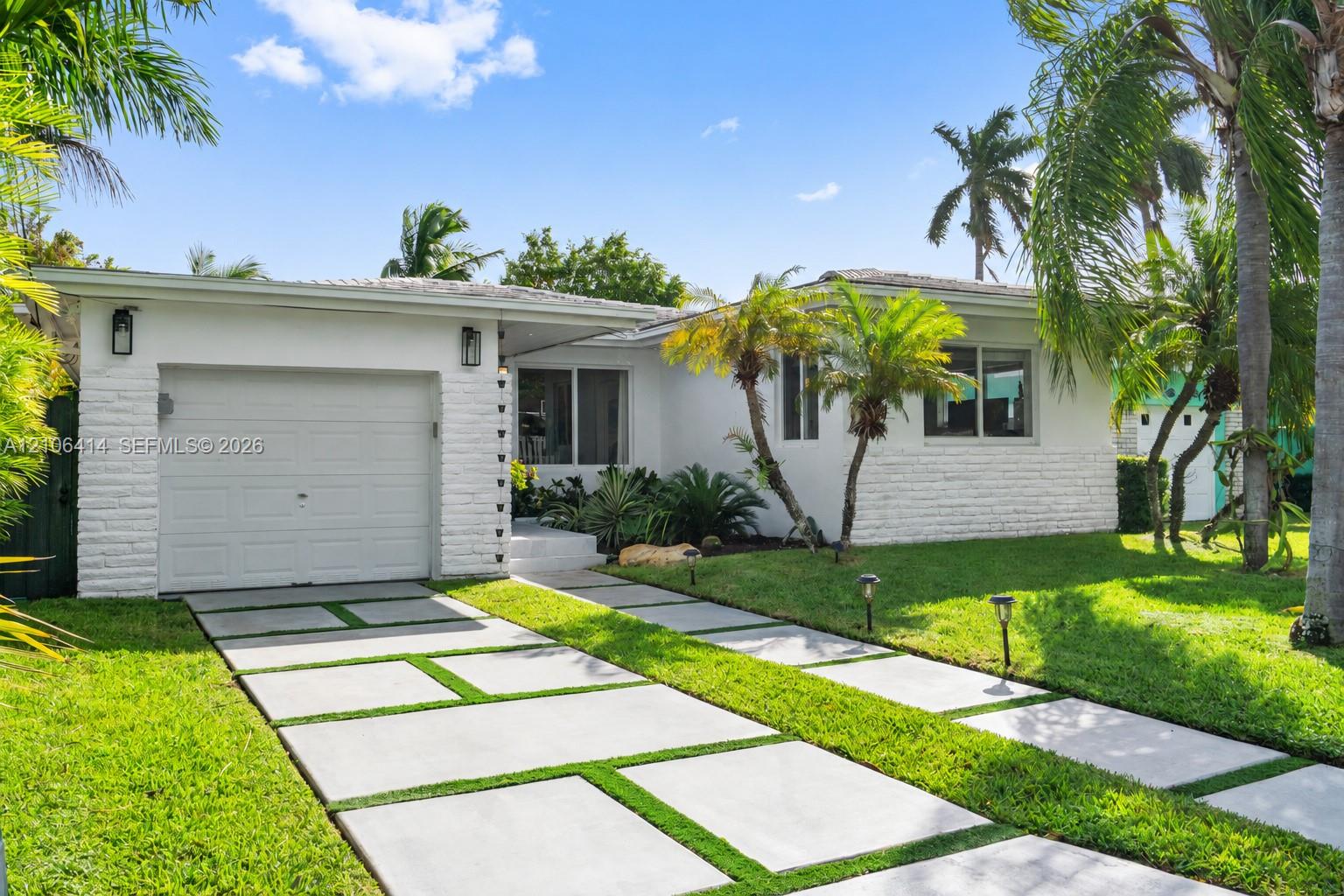 Exterior featuring a white painted brick facade, single-car garage, and a geometric concrete paver driveway with integrated turf
