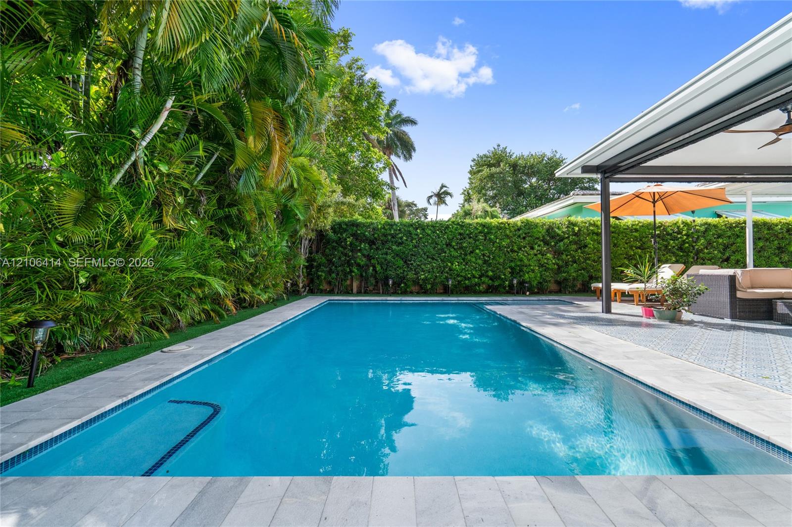 In-ground swimming pool with stone-tiled decking, covered patio with patterned flooring, and perimeter privacy hedging In-ground swimming pool with stone-tiled decking, covered patio with patterned flooring, and perimeter privacy hedging