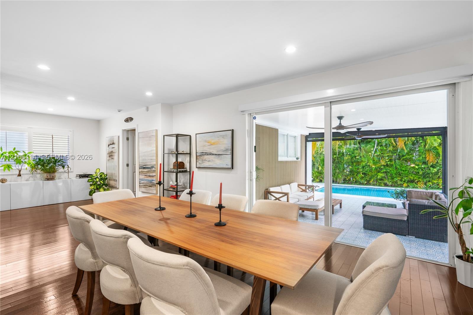 Open-concept dining area featuring wood-finish flooring, recessed lighting, white built-in cabinetry, and large sliding glass doors providing access to a covered patio and swimming pool