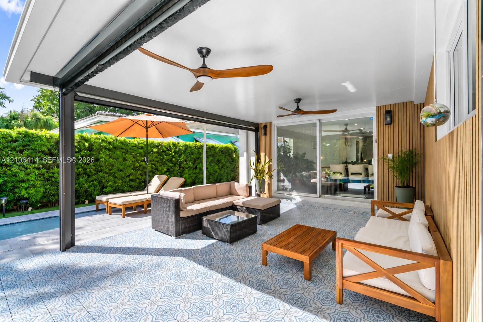 Covered patio featuring patterned tile flooring, wood-slat accent wall, and two ceiling fans