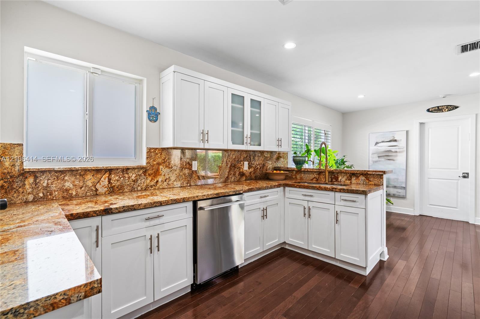 Kitchen featuring white cabinetry with glass-front uppers, stone countertops, stone backsplash, stainless steel dishwasher, and wood-finish flooring