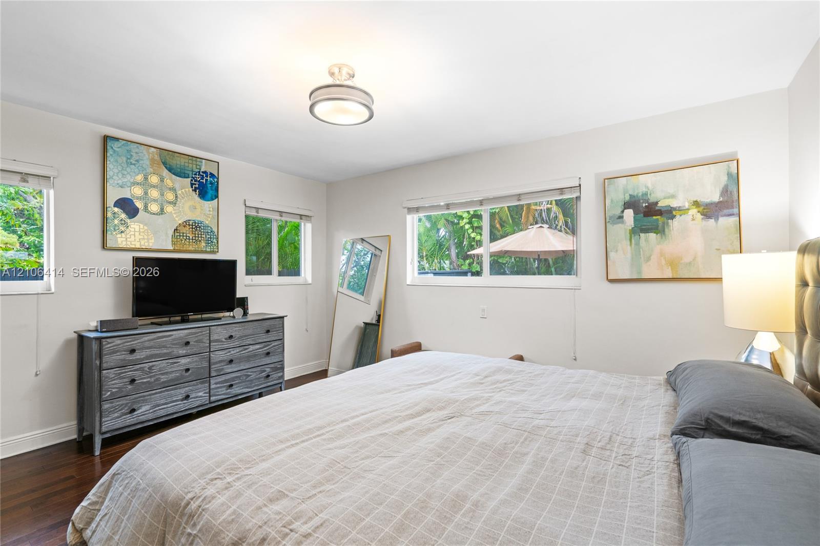Bedroom interior featuring dark wood-finish flooring, multi-pane windows, and a circular drum flush-mount light fixture