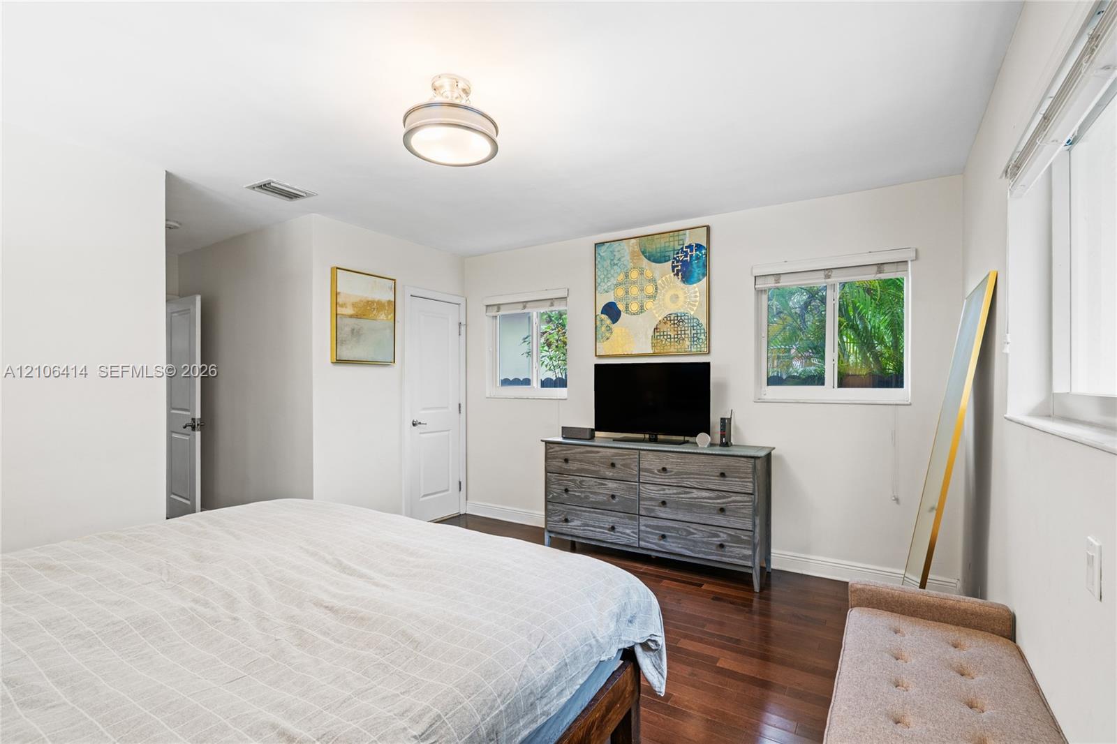 Room with dark wood-finish flooring, two dual-pane windows with horizontal blinds, and a flush-mount circular ceiling light fixture