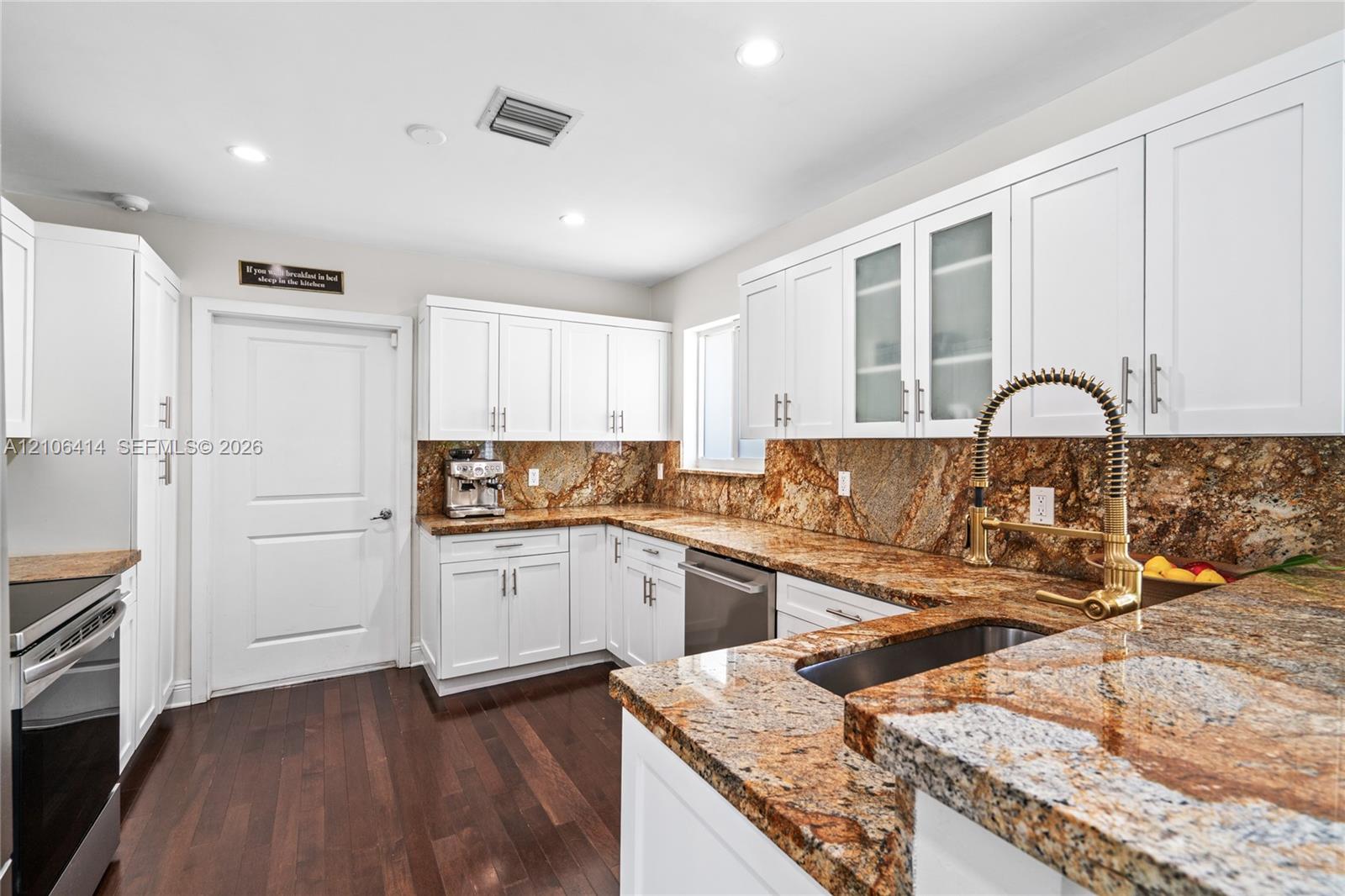 Kitchen featuring white shaker-style cabinetry, natural stone countertops with integrated backsplash, wood-finish flooring, undermount sink with high-arc pull-down faucet, and stainless steel appliances